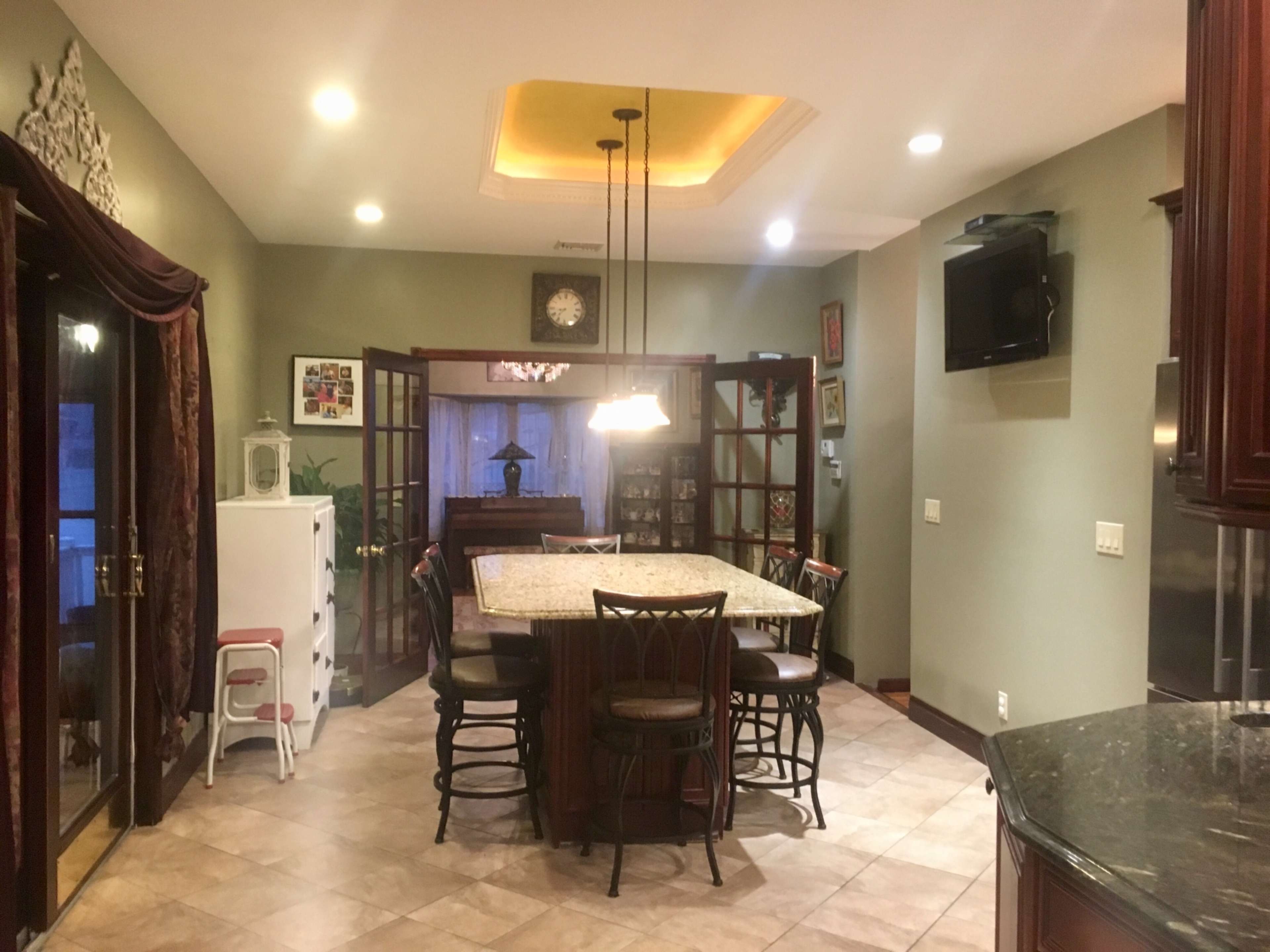 A spacious kitchen features a large island with seating, surrounded by cabinets and a dining area, illuminated by pendant lights.
