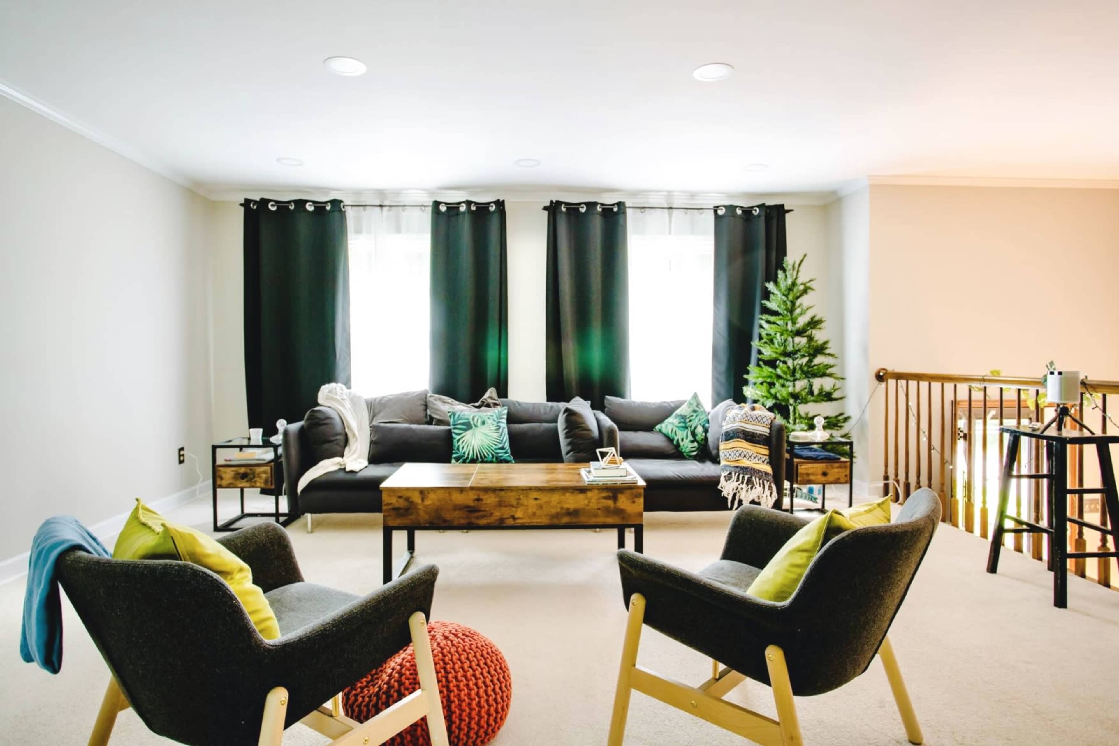 The scene features a cozy living room with a gray sofa, two modern chairs, a wooden coffee table, and a small Christmas tree in the corner.