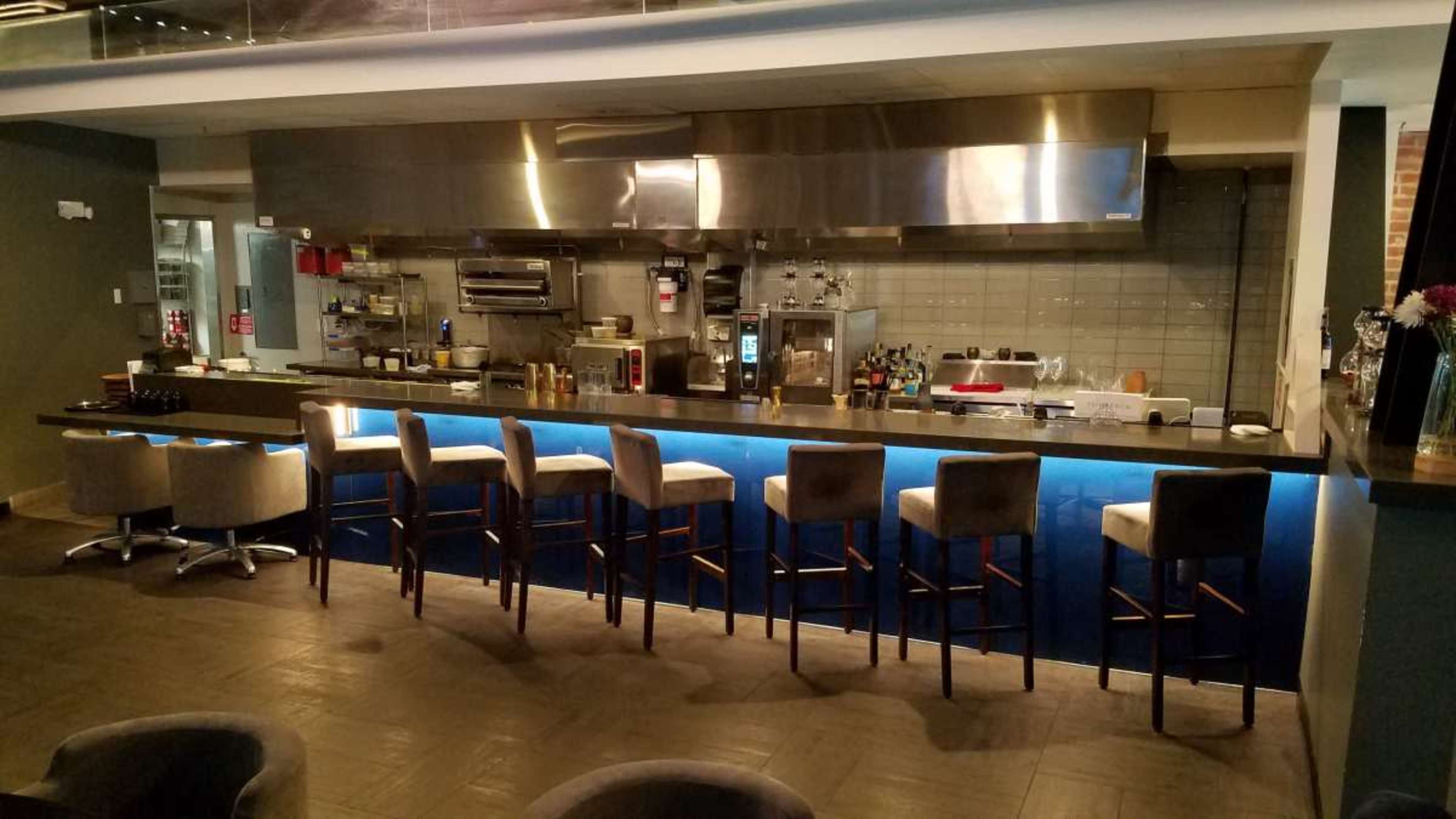 The image shows a modern kitchen area with a bar counter featuring high stools, illuminated by blue lighting.