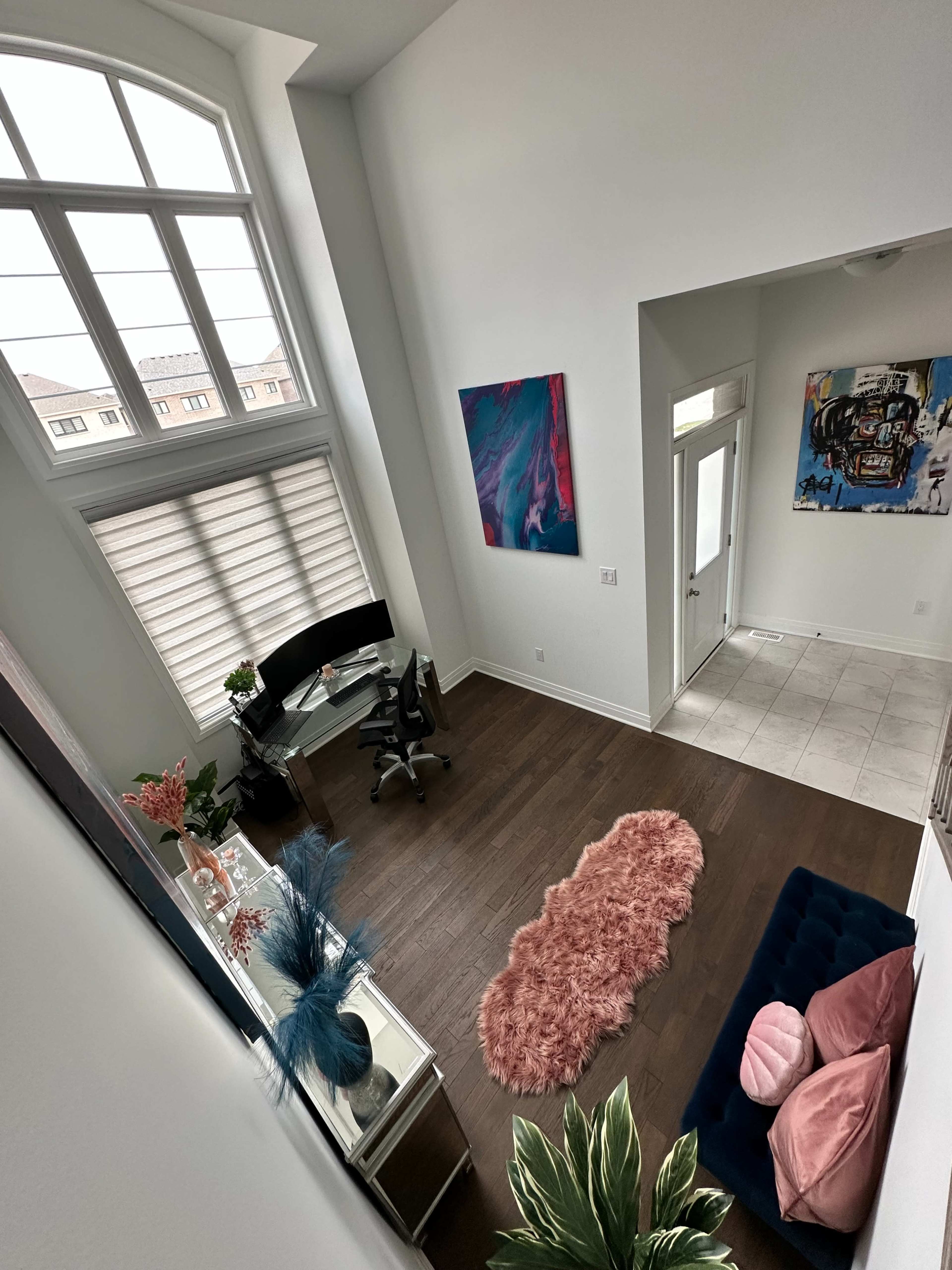 A bright, airy room with large windows, featuring a desk and chair, a plush rug, and colorful artwork on the walls.