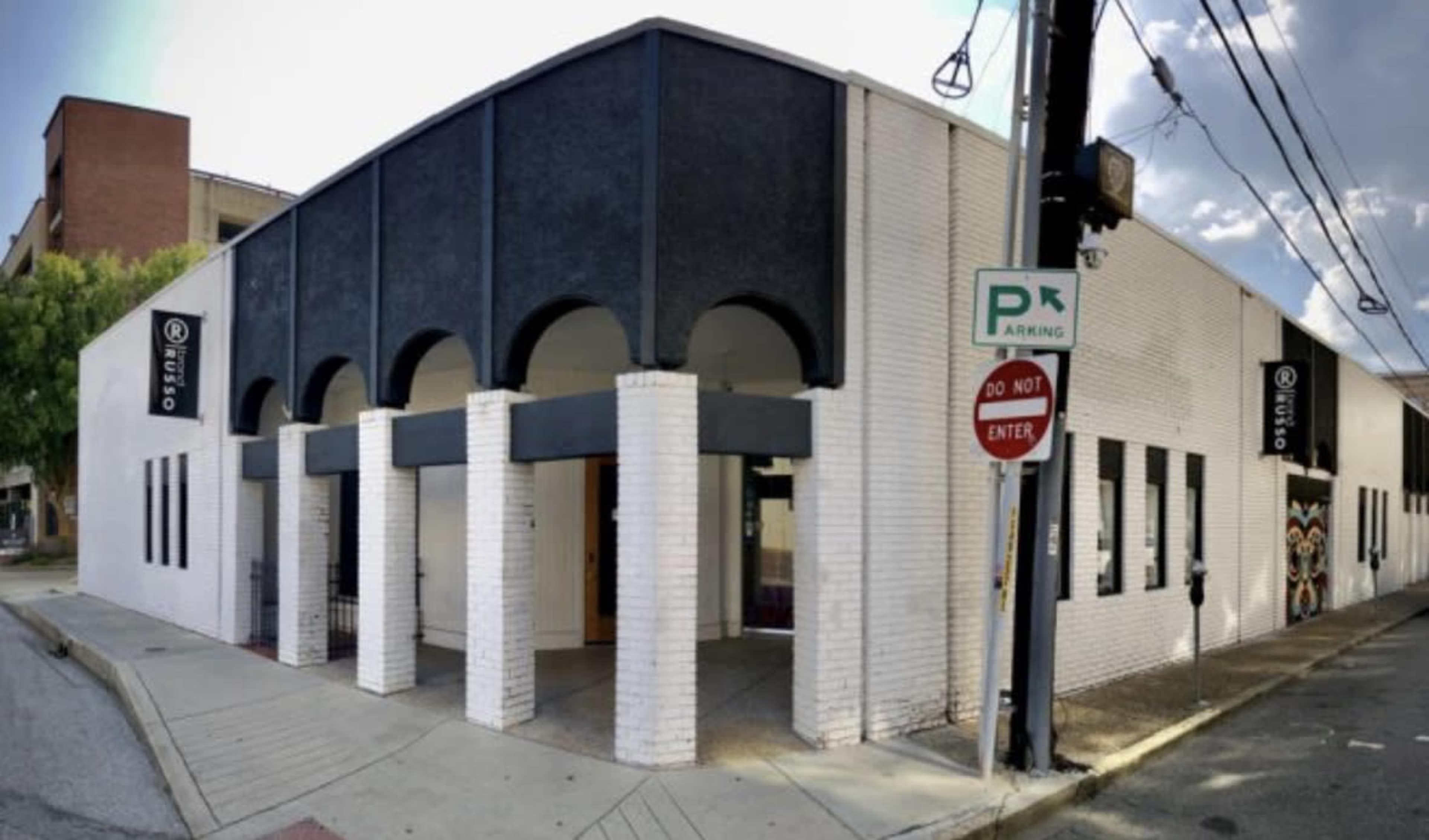 A modern, white brick building with a black, arched facade and large entrance, located at a street corner.