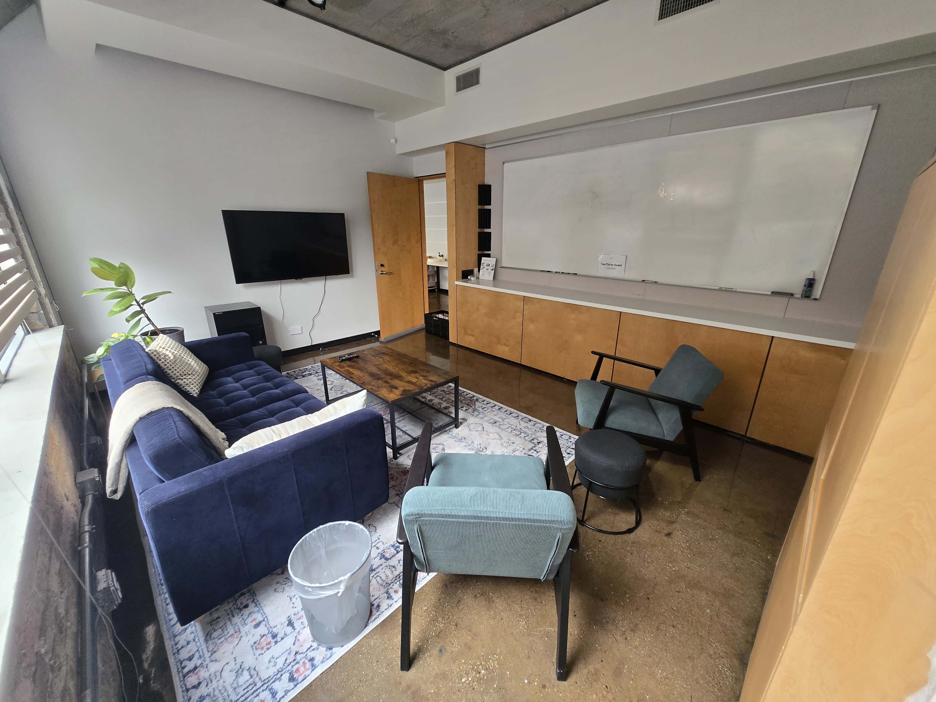 The image shows a modern office space featuring a seating area with a blue couch, two chairs, a coffee table, and a whiteboard on one wall.