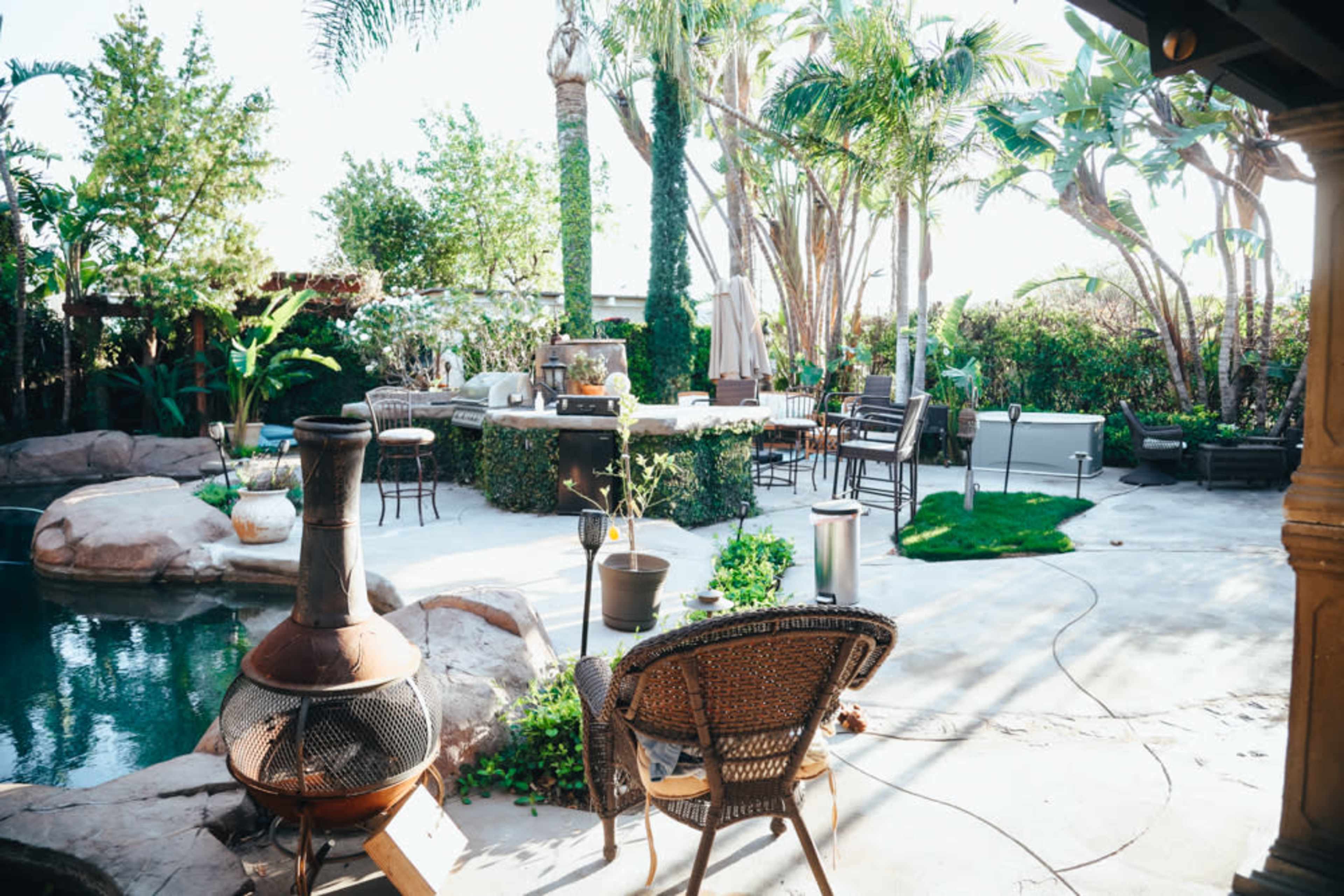 A landscaped backyard with a pool, outdoor seating, a barbecue area, and various tropical plants.