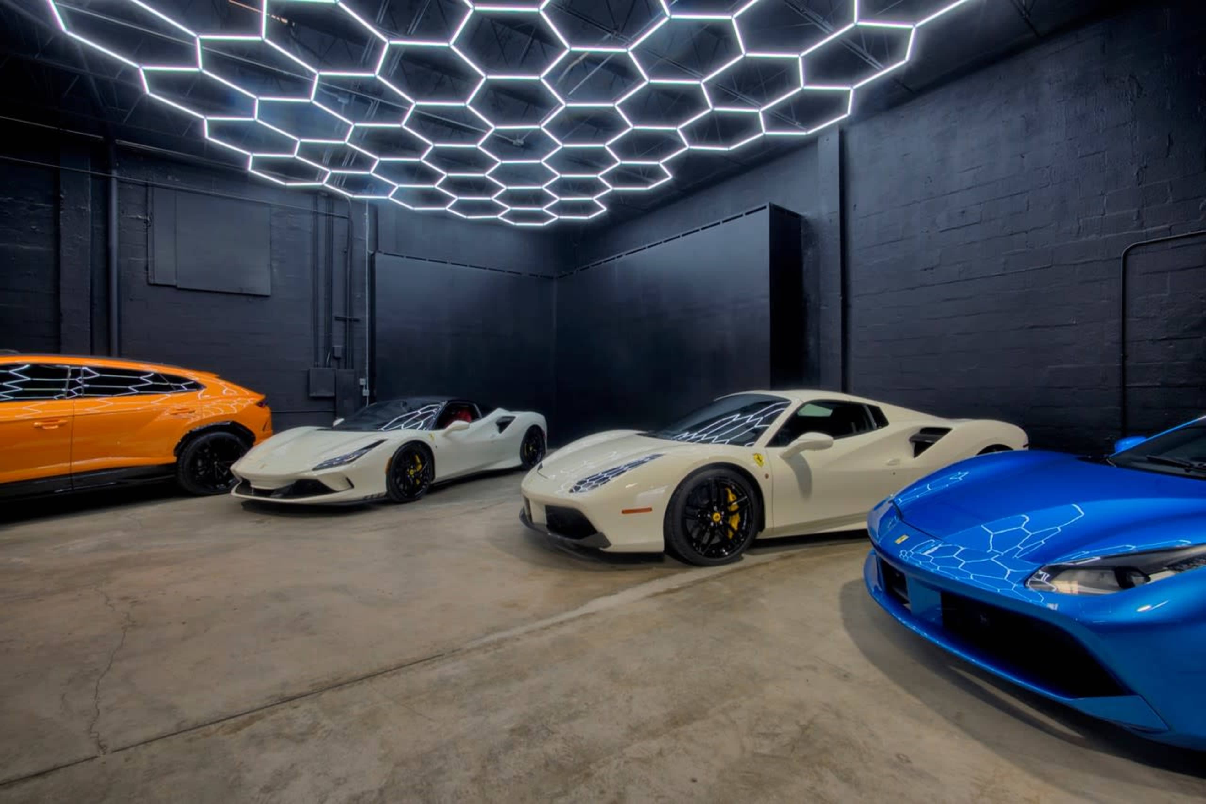 A modern garage featuring four luxury cars under a hexagonal LED light ceiling.