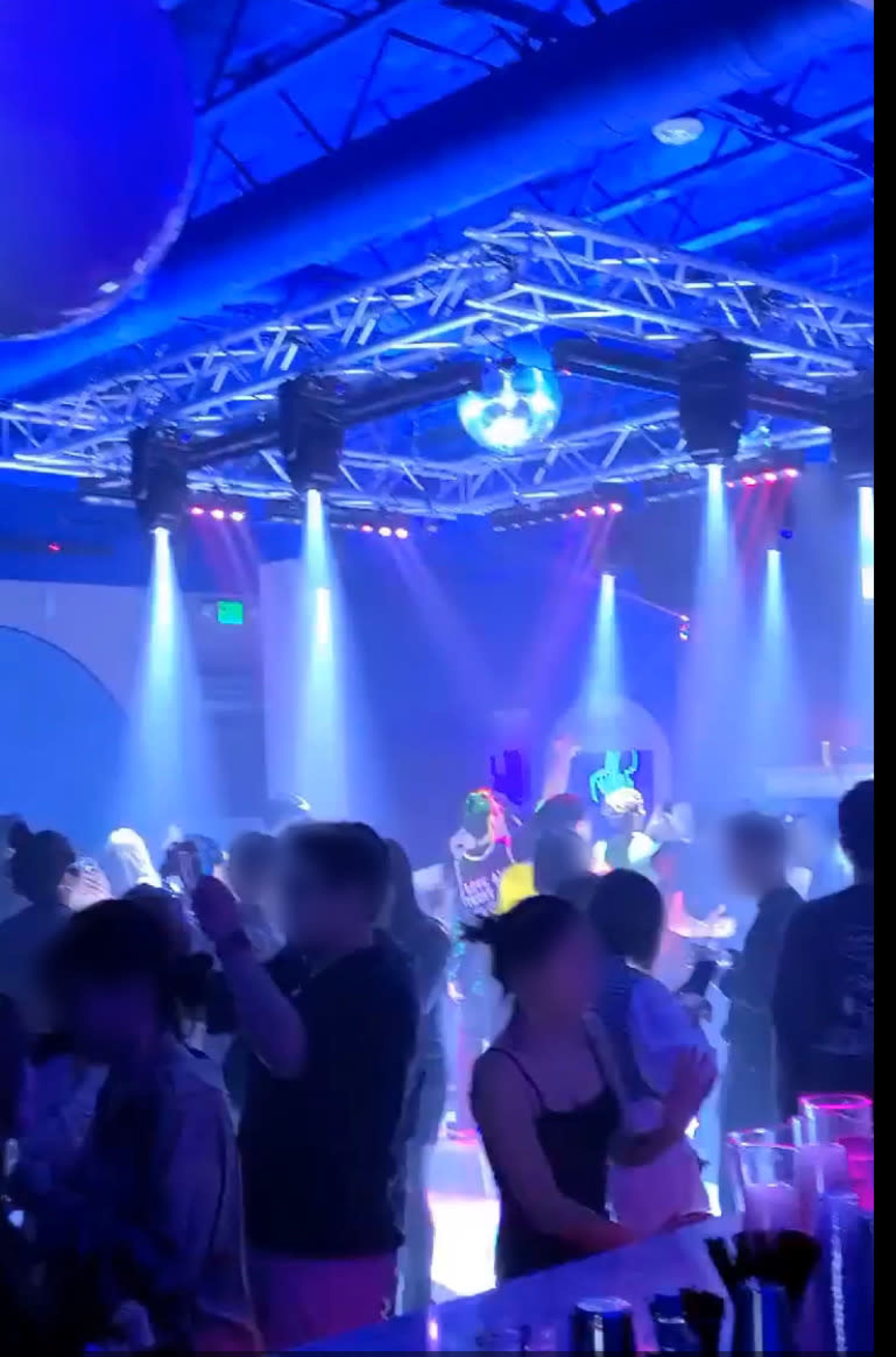 A crowded party scene with people dancing under colorful lights and a disco ball.