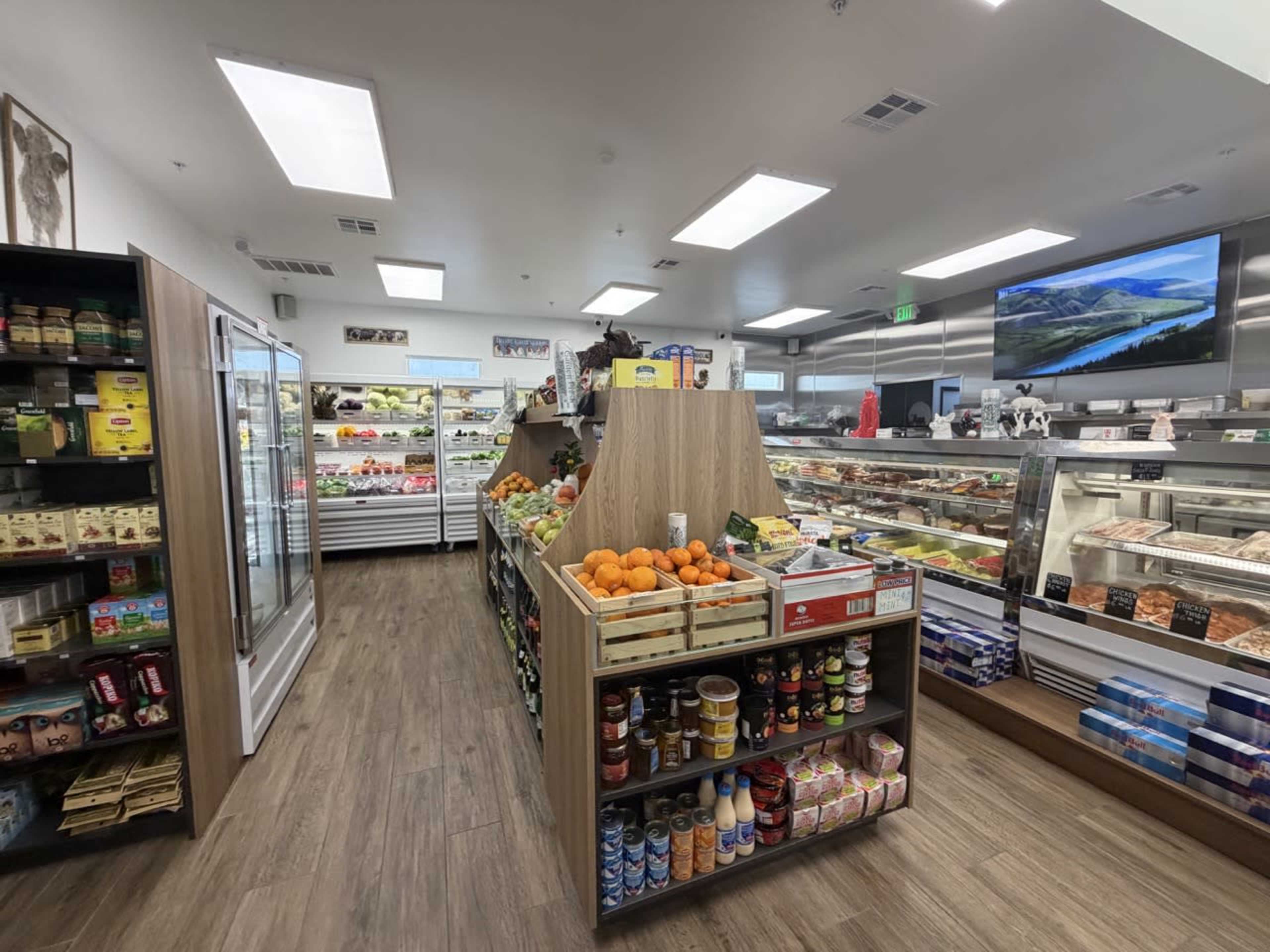 The image shows the interior of a grocery store featuring neatly arranged displays of fresh produce, refrigerated items, and canned goods.