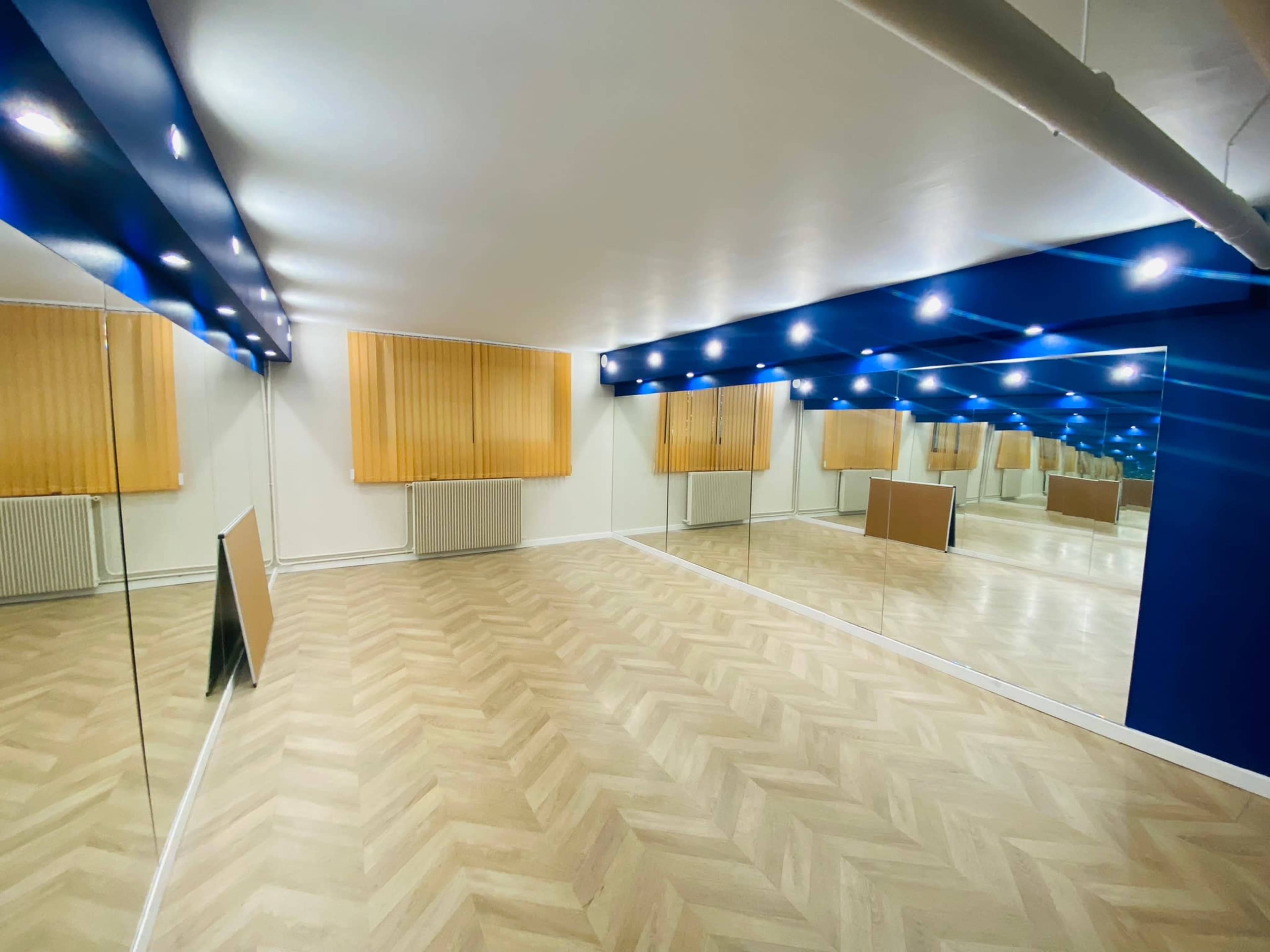 A spacious room with hardwood flooring, blue ceiling lights, and mirror walls.