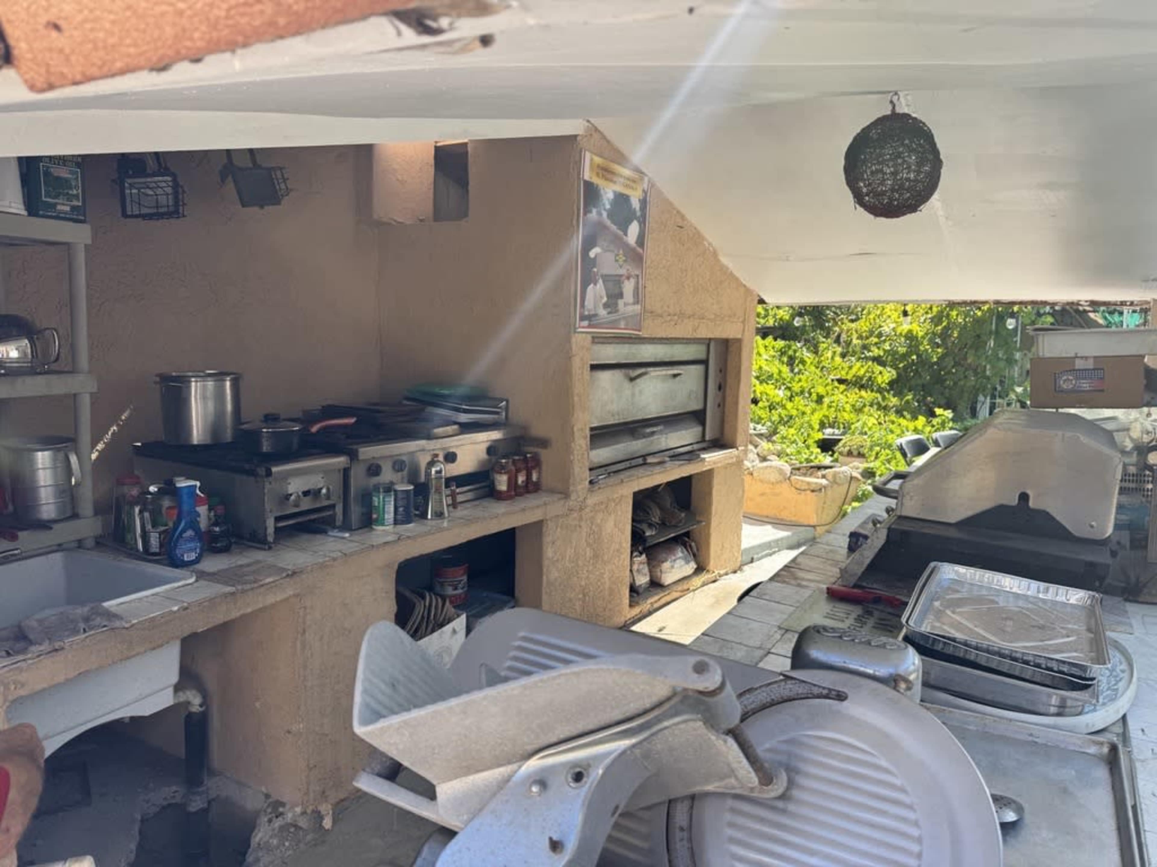 The image shows an outdoor kitchen area with cooking equipment, countertops, and various utensils arranged on shelves.