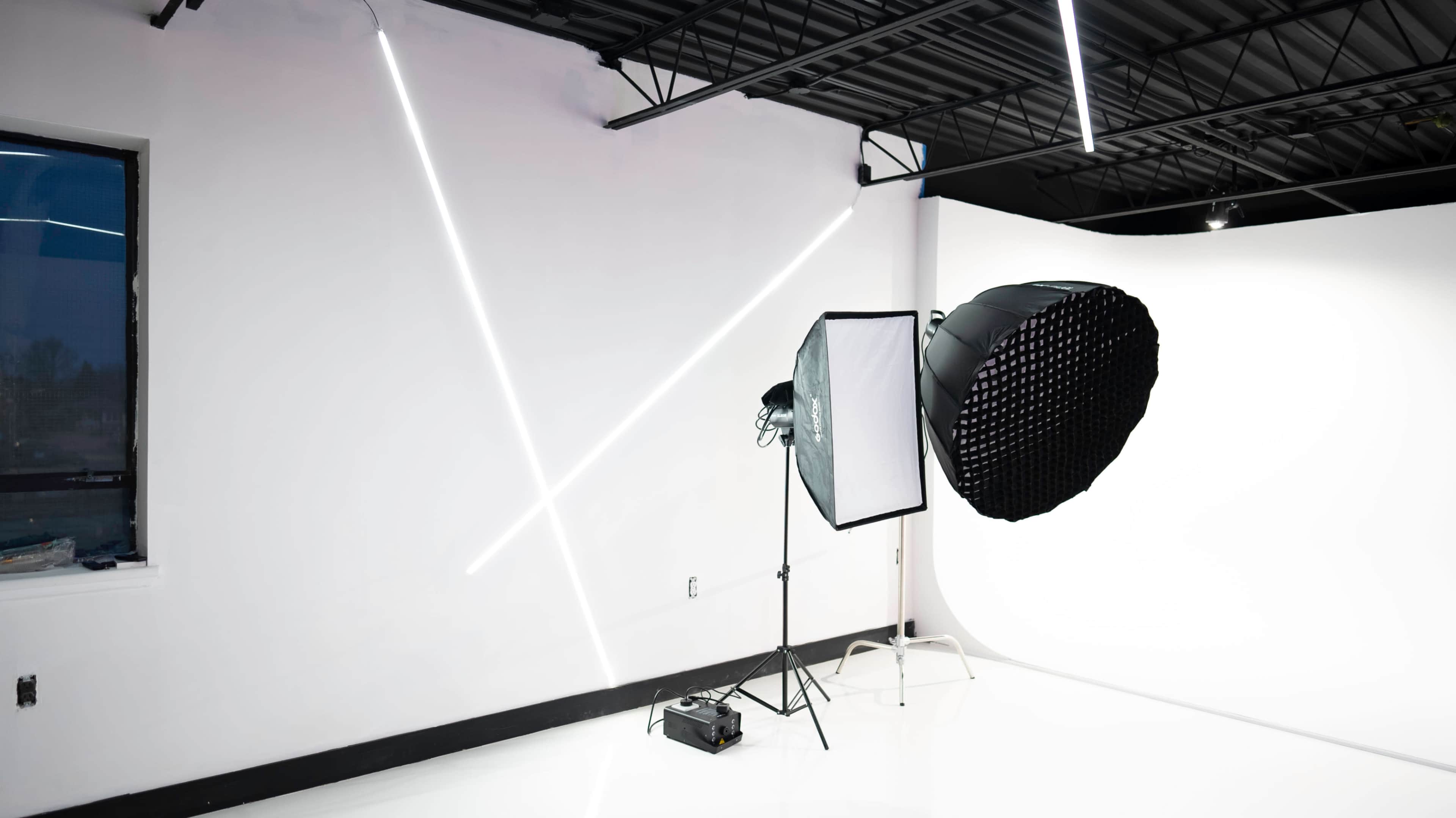 A photography studio with a large softbox light and a grid light set up against a white backdrop, illuminated by modern linear lights on the walls.