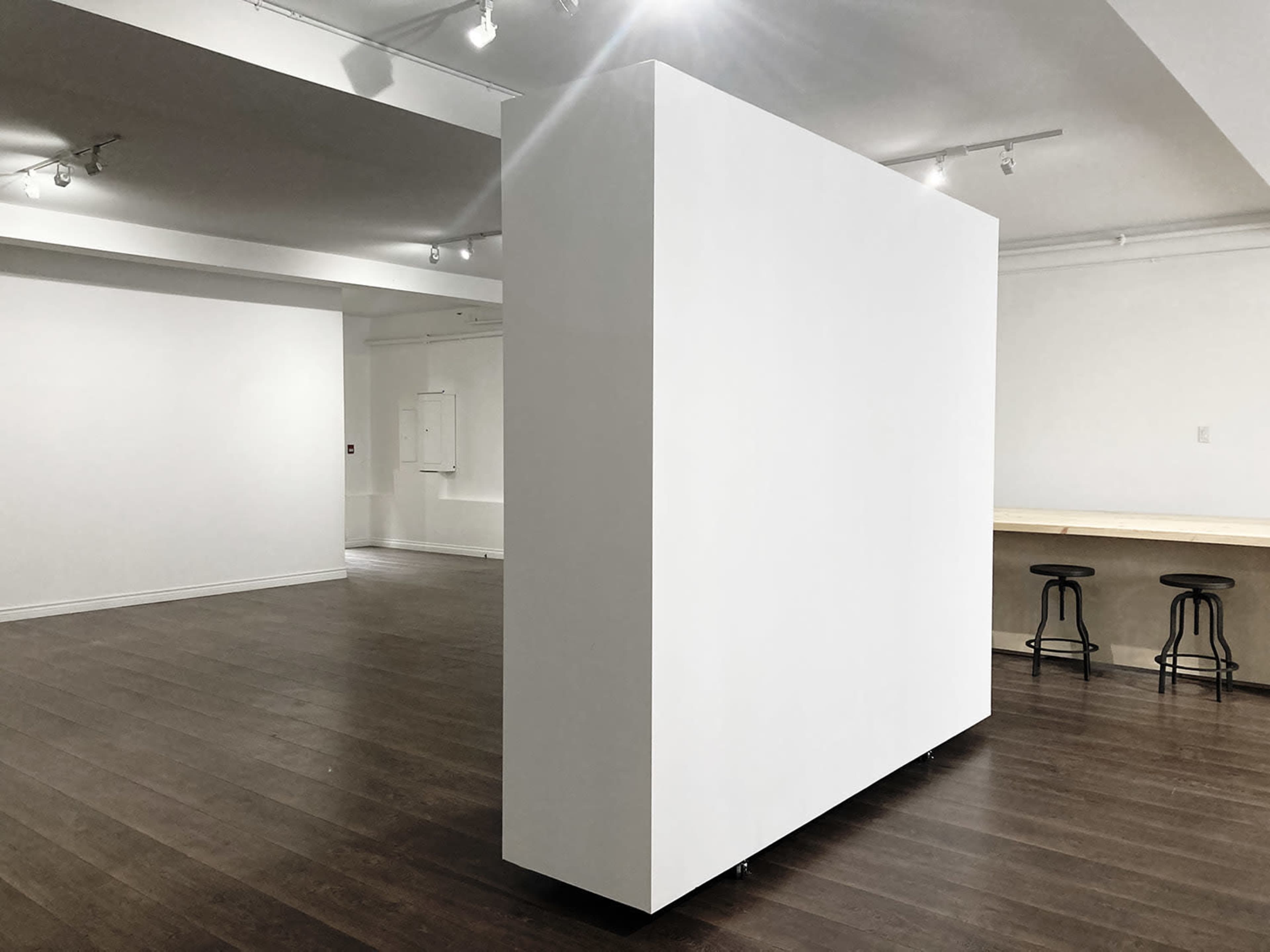 A spacious, minimalist room featuring a large white partition and wooden seating along one wall.