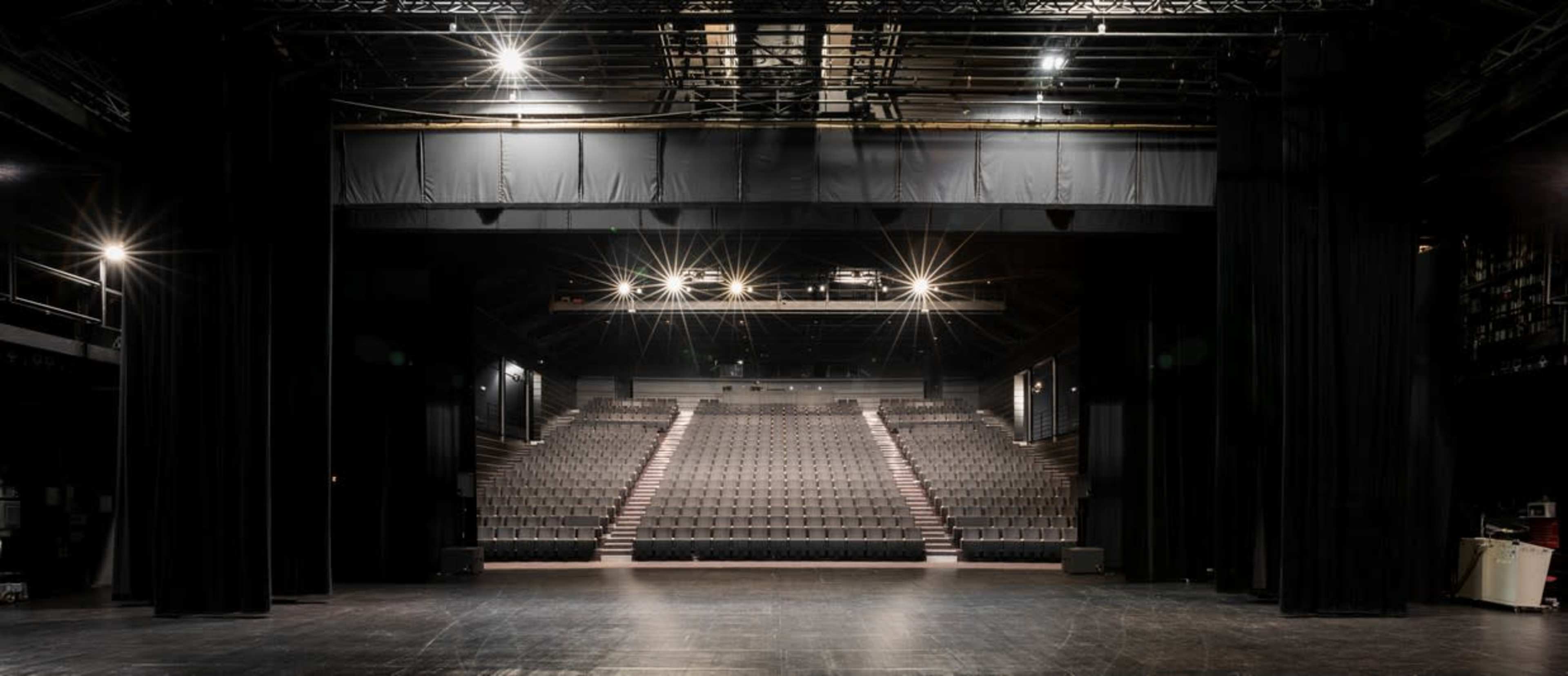 The image shows a dimly lit theater with rows of empty seats facing a stage.