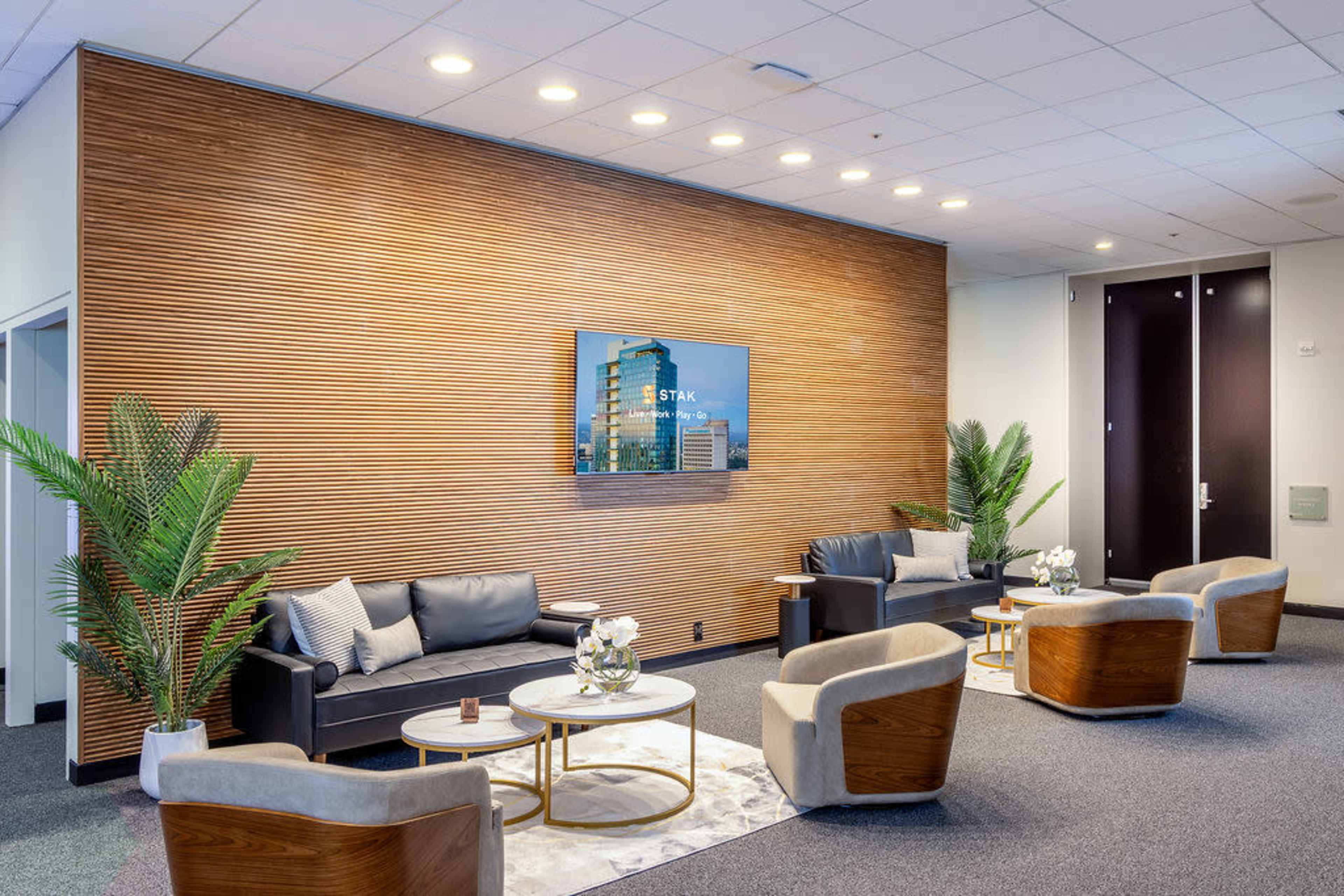 The image shows a modern lounge area with a wooden accent wall, leather sofas, armchairs, a coffee table, and a television mounted above.