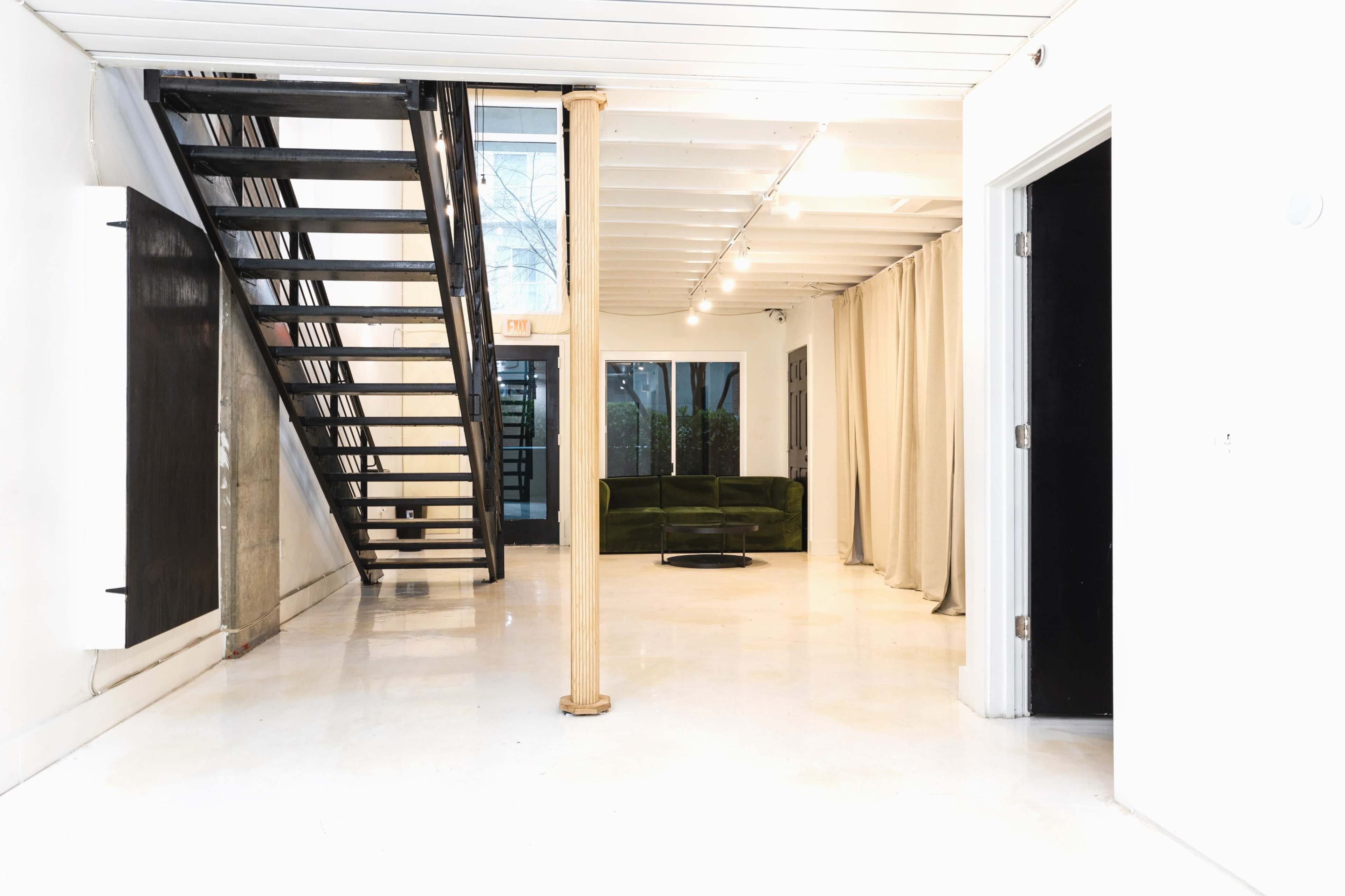 A modern interior space featuring a staircase on the left, a green sofa, and an open layout with polished floors and large windows.