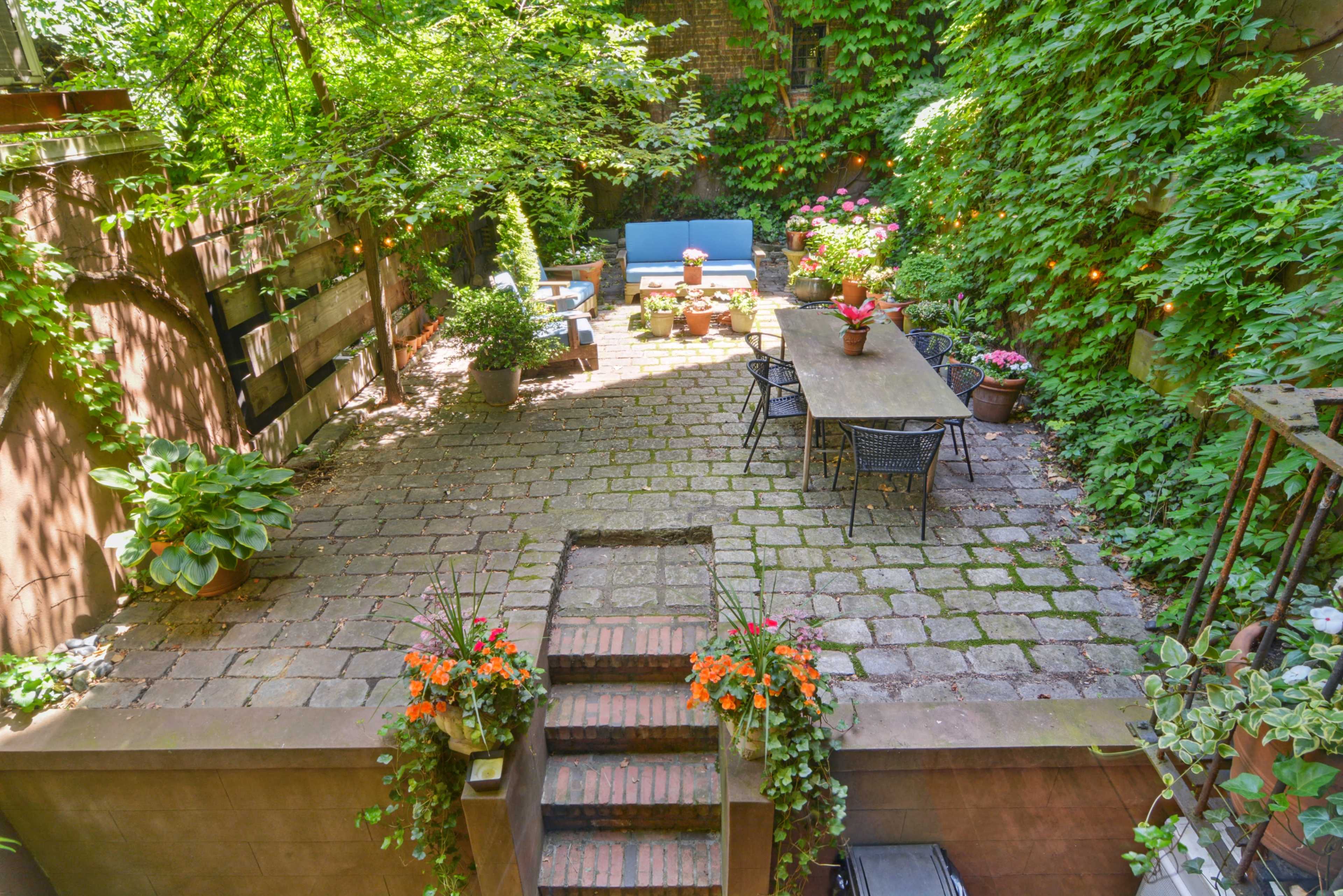A stone-paved courtyard surrounded by lush greenery, featuring seating areas with potted plants.