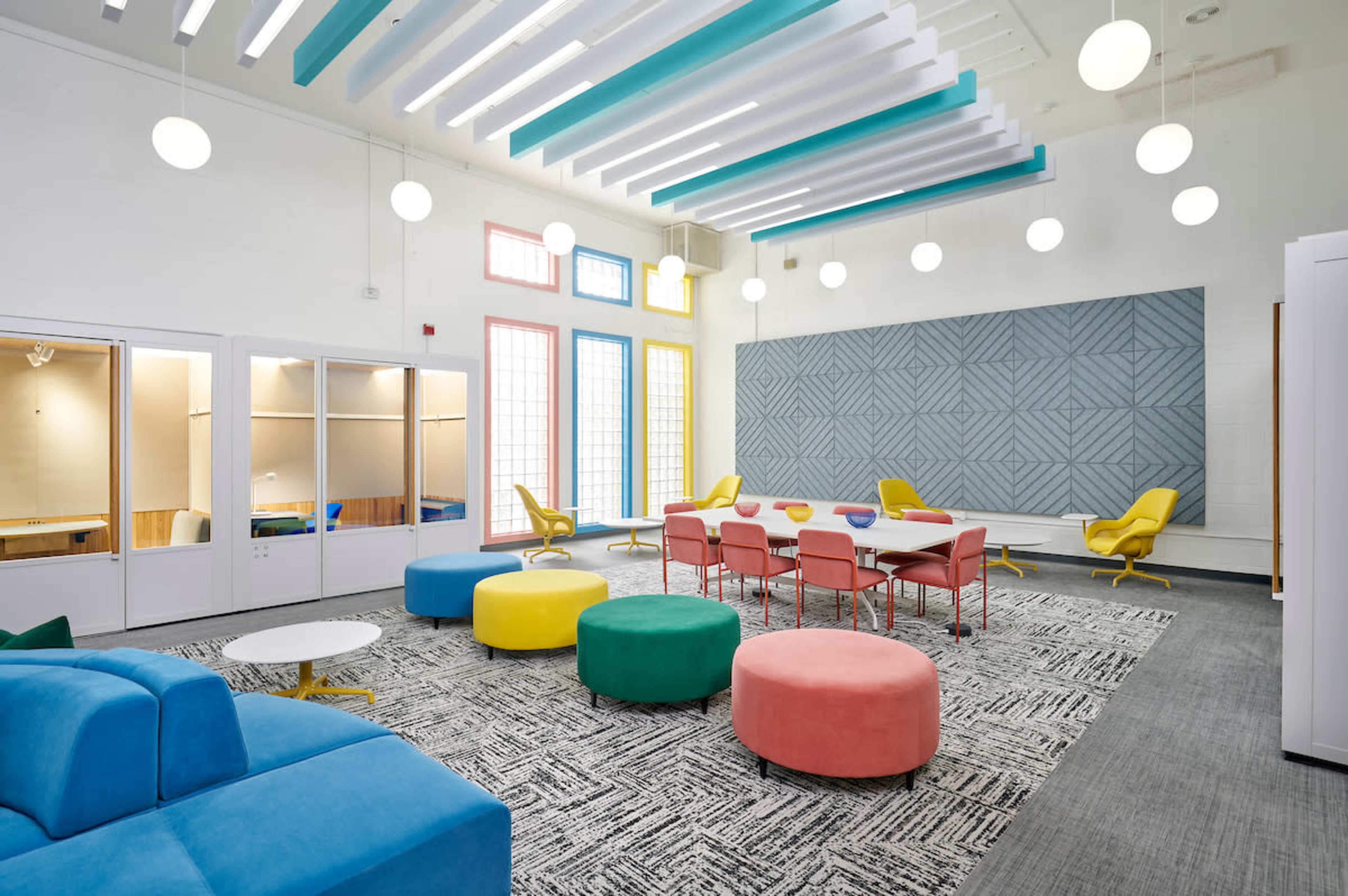A brightly colored modern lounge featuring various seating options, a large table, and decorative light fixtures.