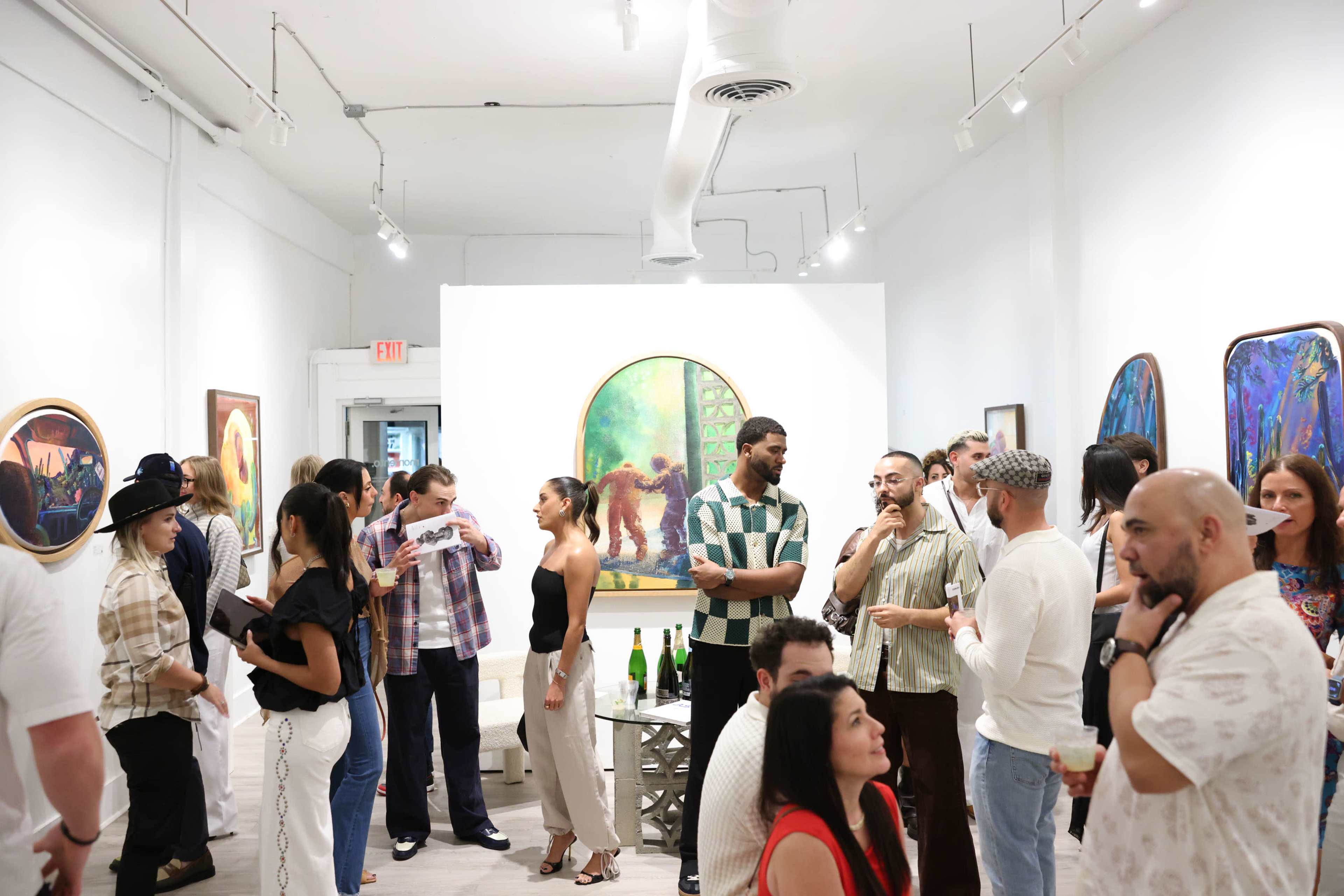A diverse group of people mingles in an art gallery surrounded by colorful paintings on the walls.