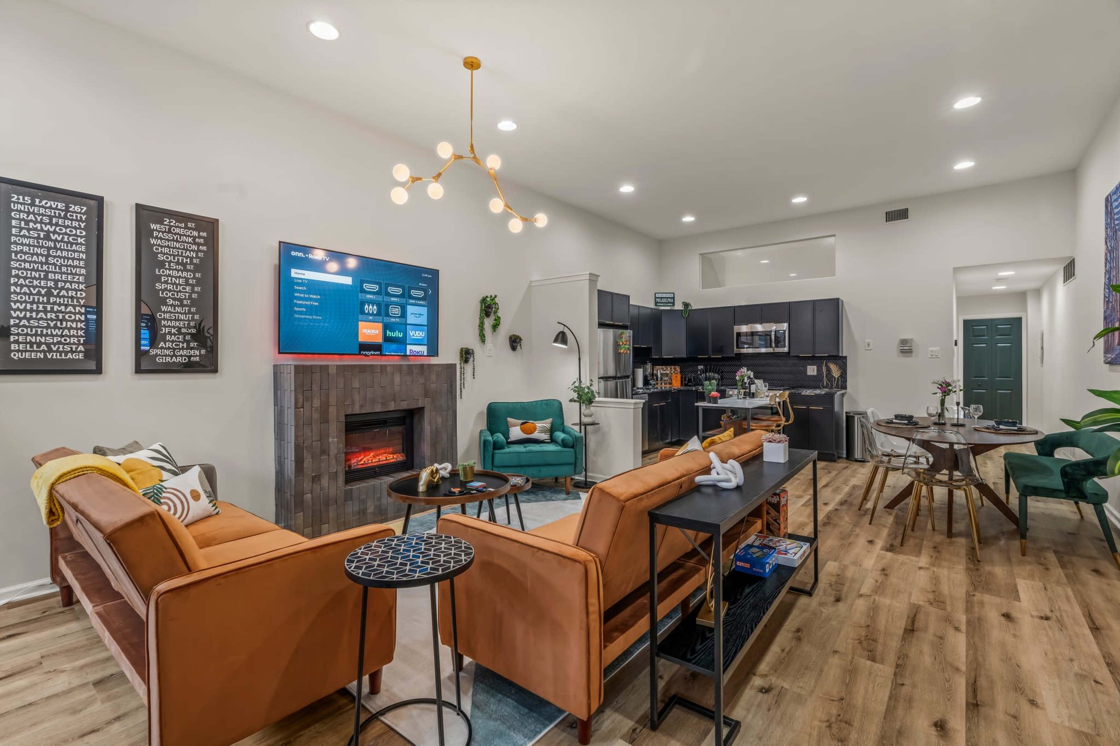 A modern living room with a television mounted on the wall, a fireplace, and contemporary furniture including a brown leather sofa, green chairs, and a wooden dining table.