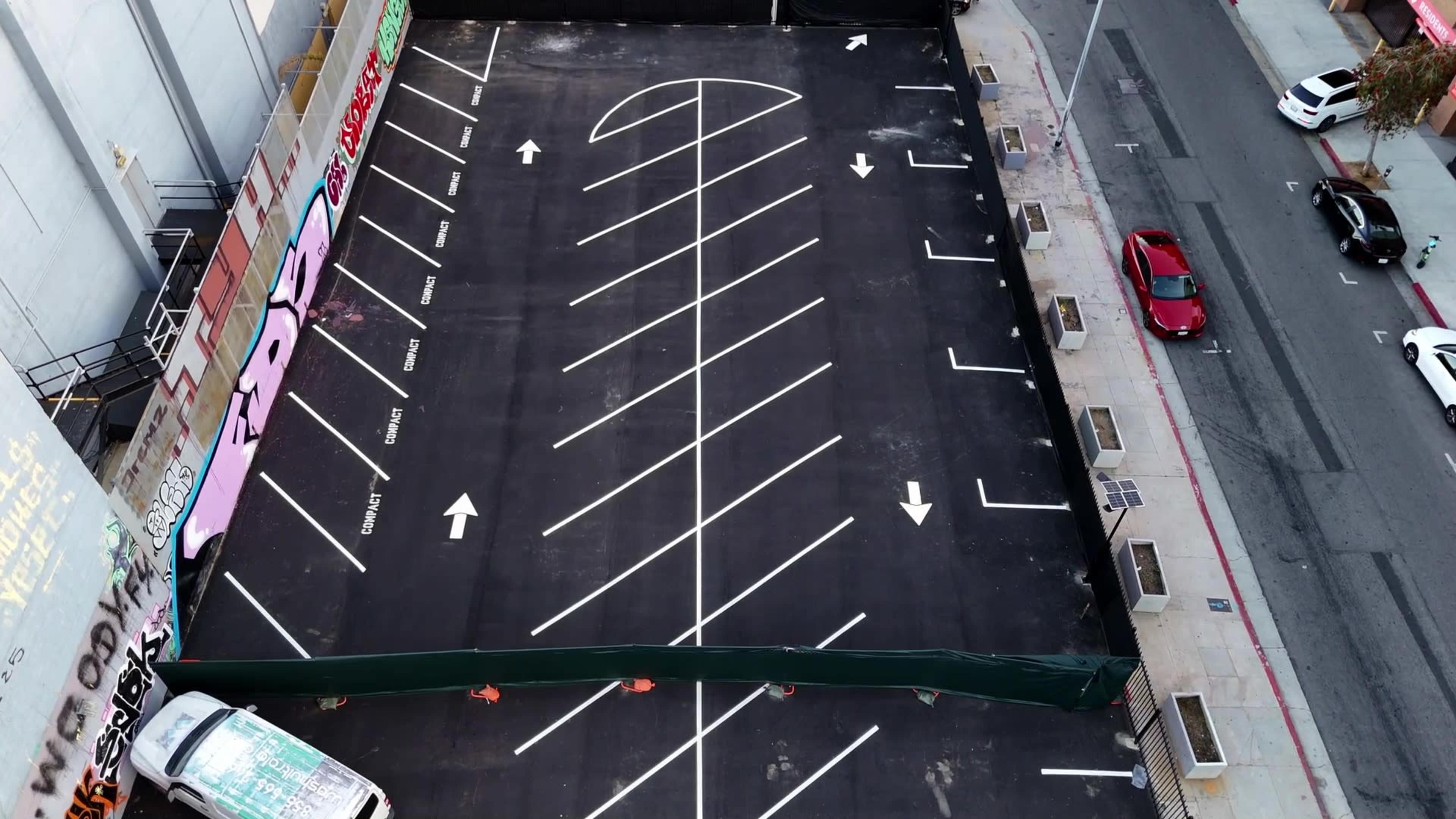 An aerial view of a nearly empty parking lot with marked spaces and directional arrows.