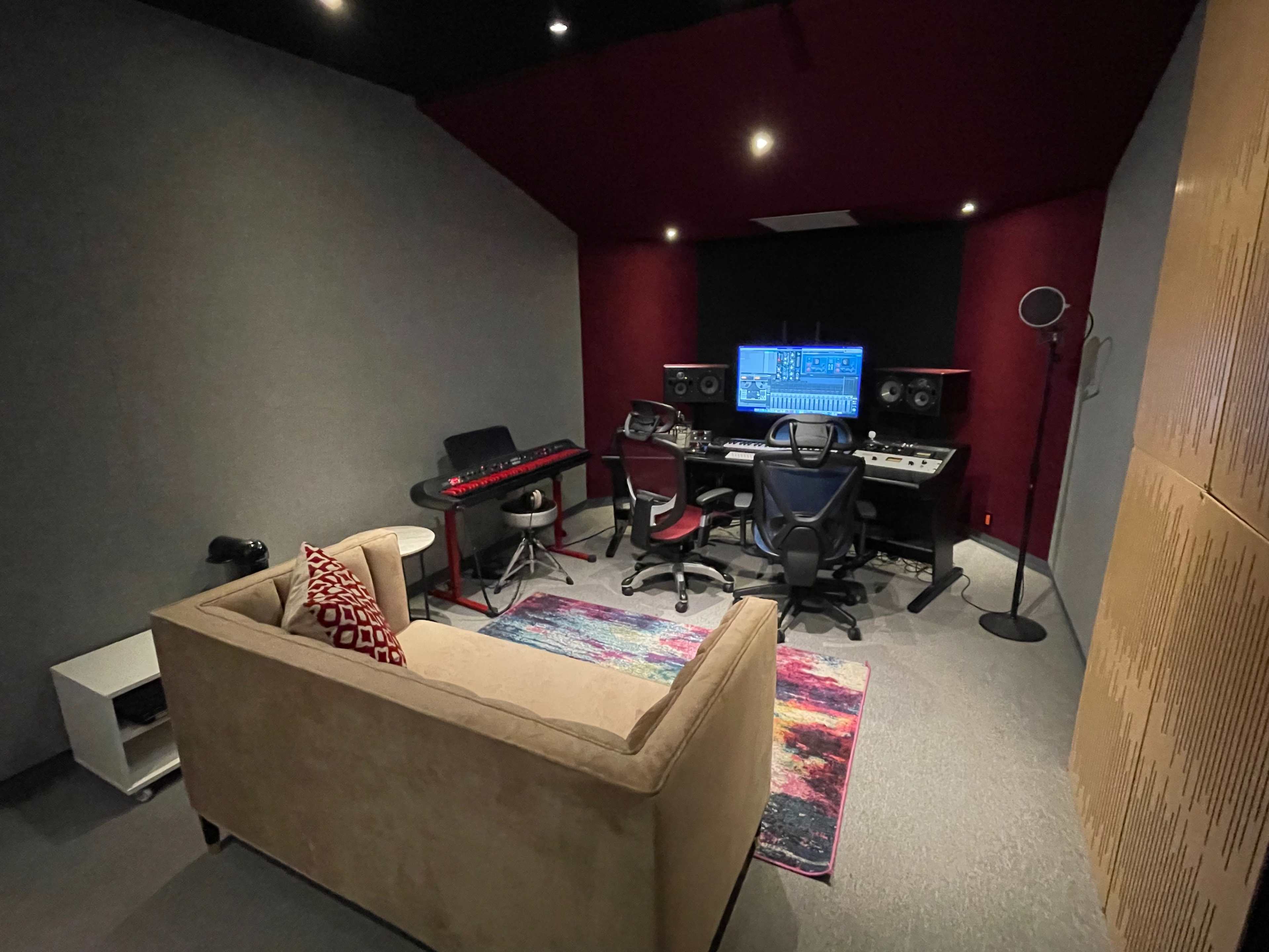 A music studio with a mixing desk, musical instruments, a chair, and a couch in a room designed for sound production.