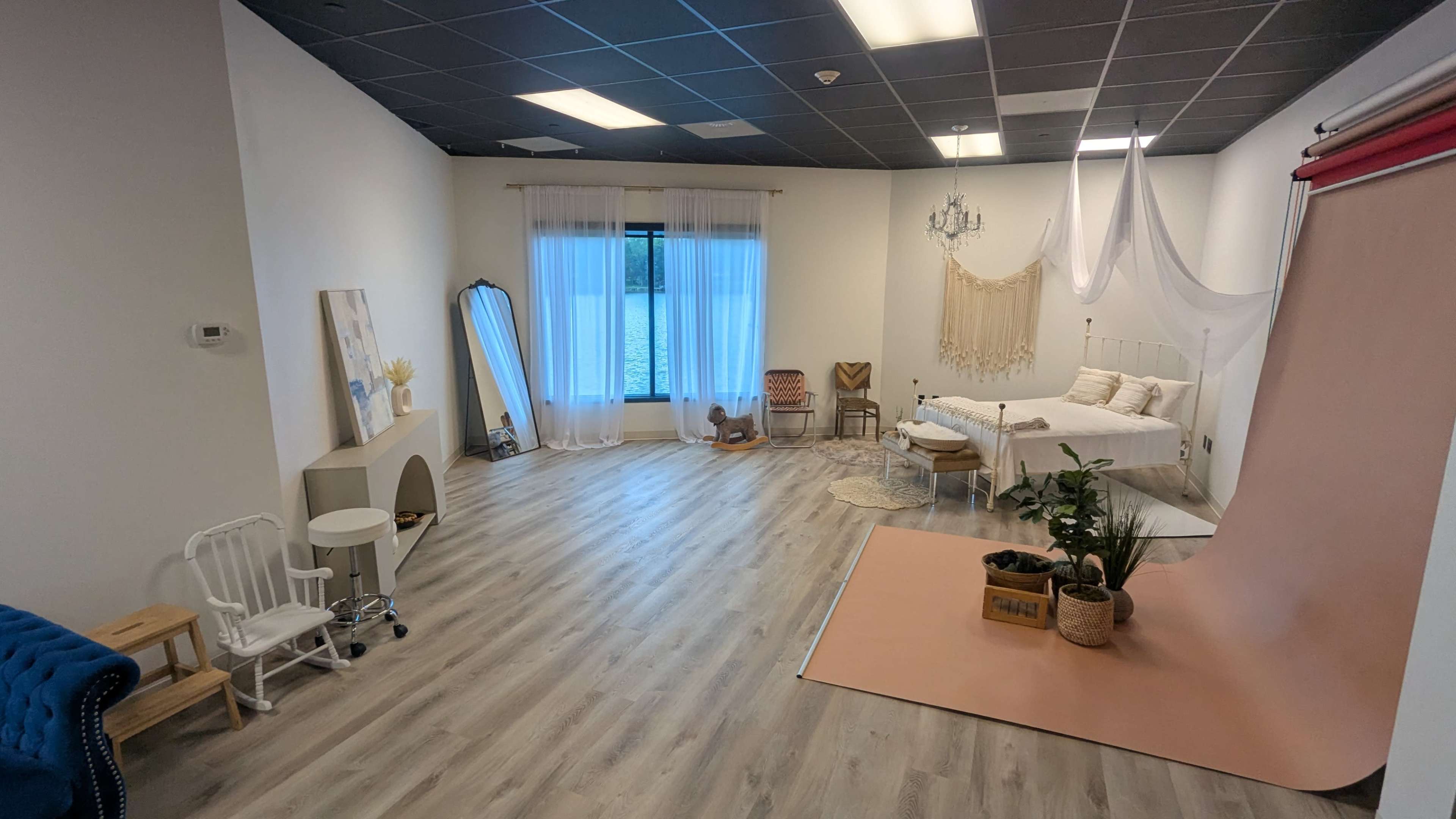 The image shows a spacious indoor studio featuring a bed, decorative textiles, a large mirror, and various furniture pieces, including a chair and a small table.