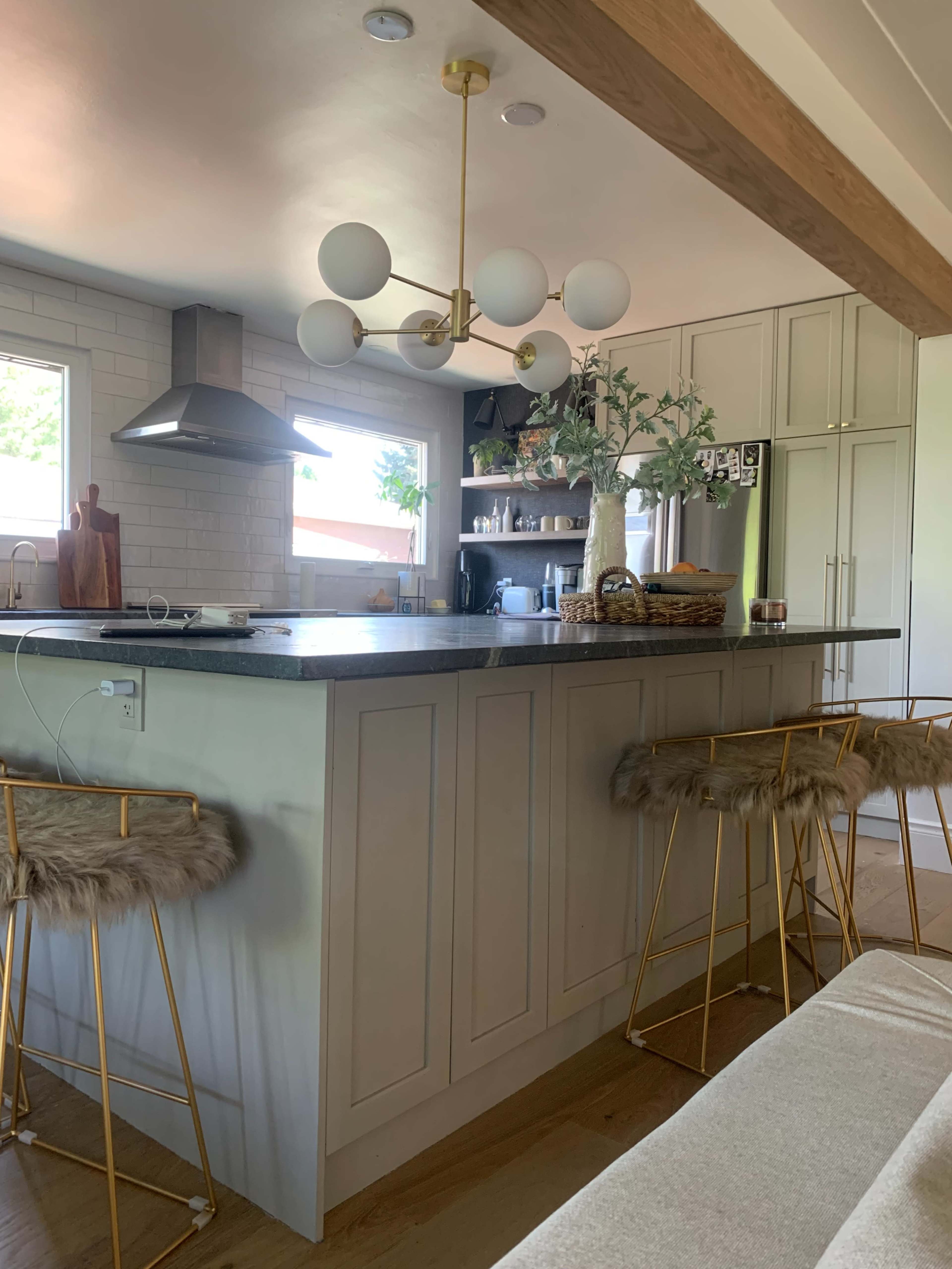 A modern kitchen with a central island, featuring bar stools, a pendant light, and organized shelves with kitchenware.