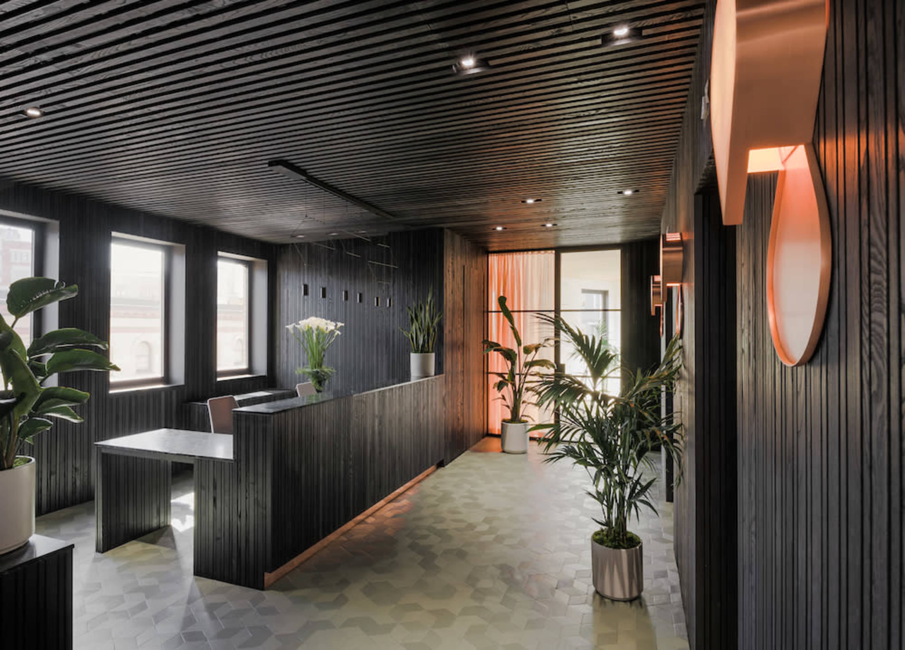 The image depicts a modern office reception area with dark wooden paneling, potted plants, and large windows.