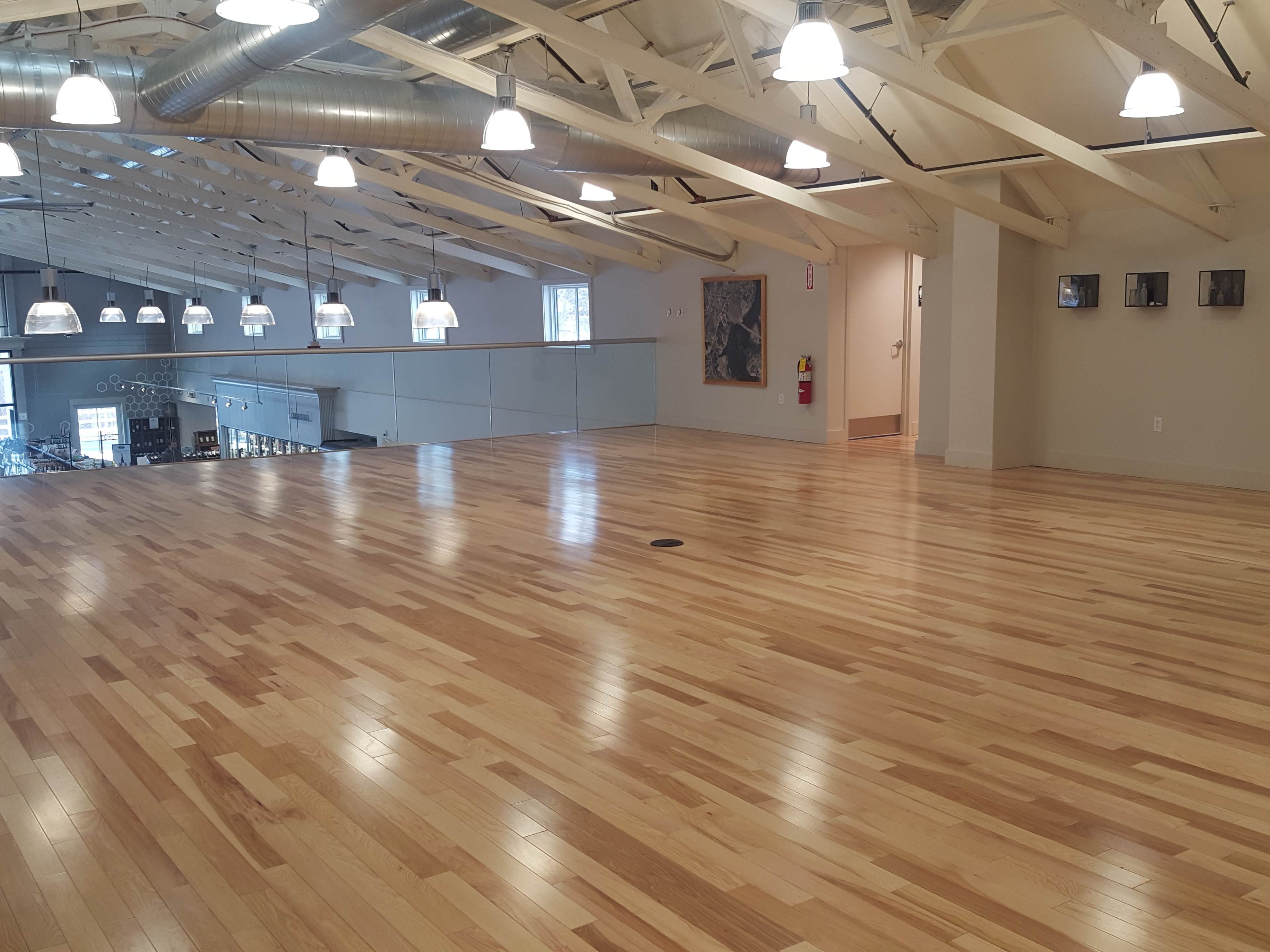 A spacious, well-lit wooden-floored room with high ceilings and industrial-style lighting.