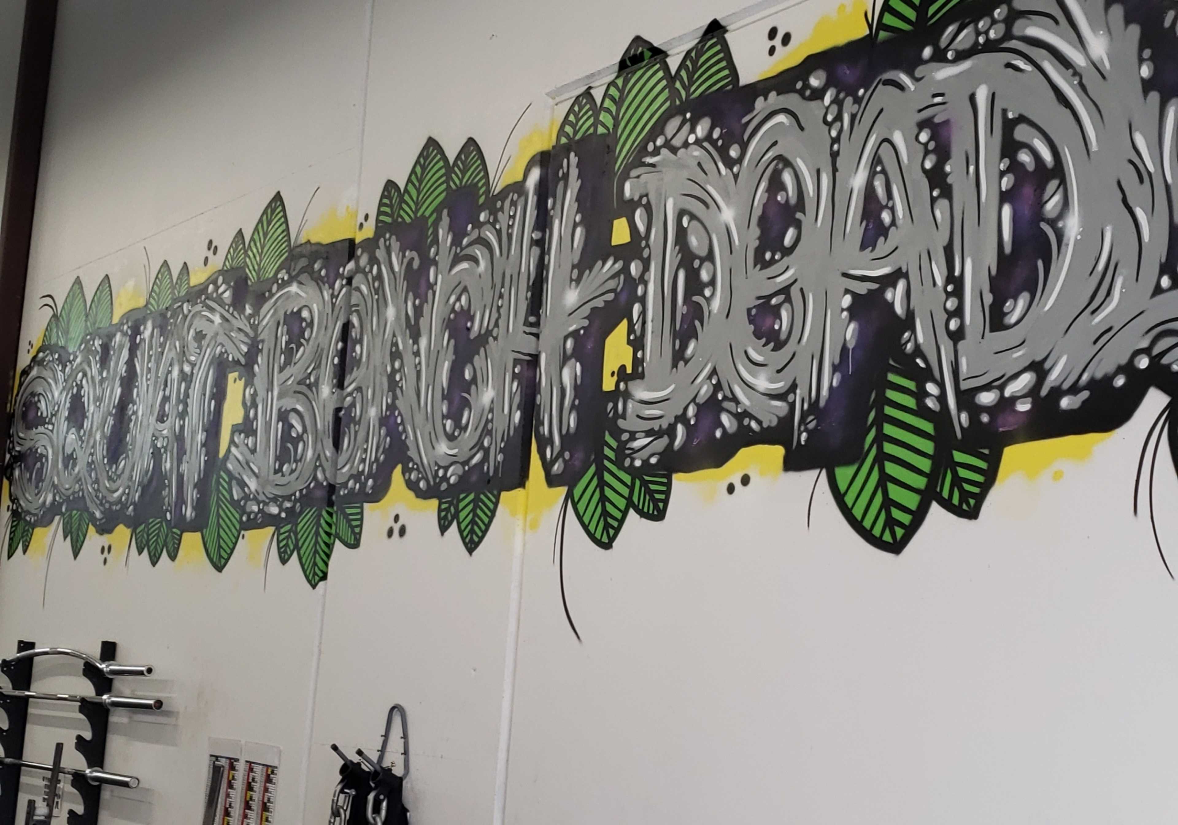 A wall mural with the words "SQUAT BENCH DEAD" decorated with green leaves.
