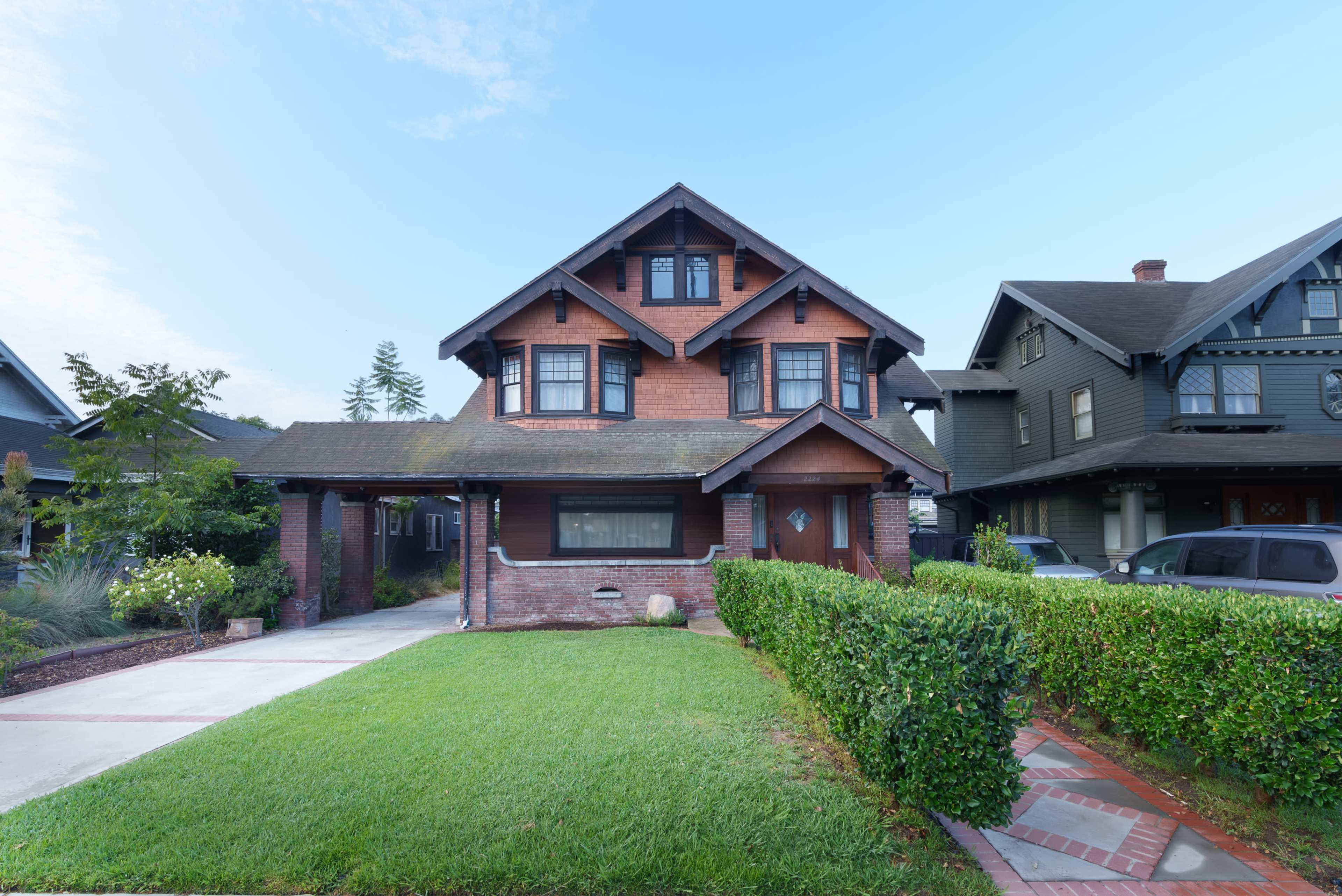 The image shows a two-story Craftsman-style house with a brick facade and a landscaped front yard.