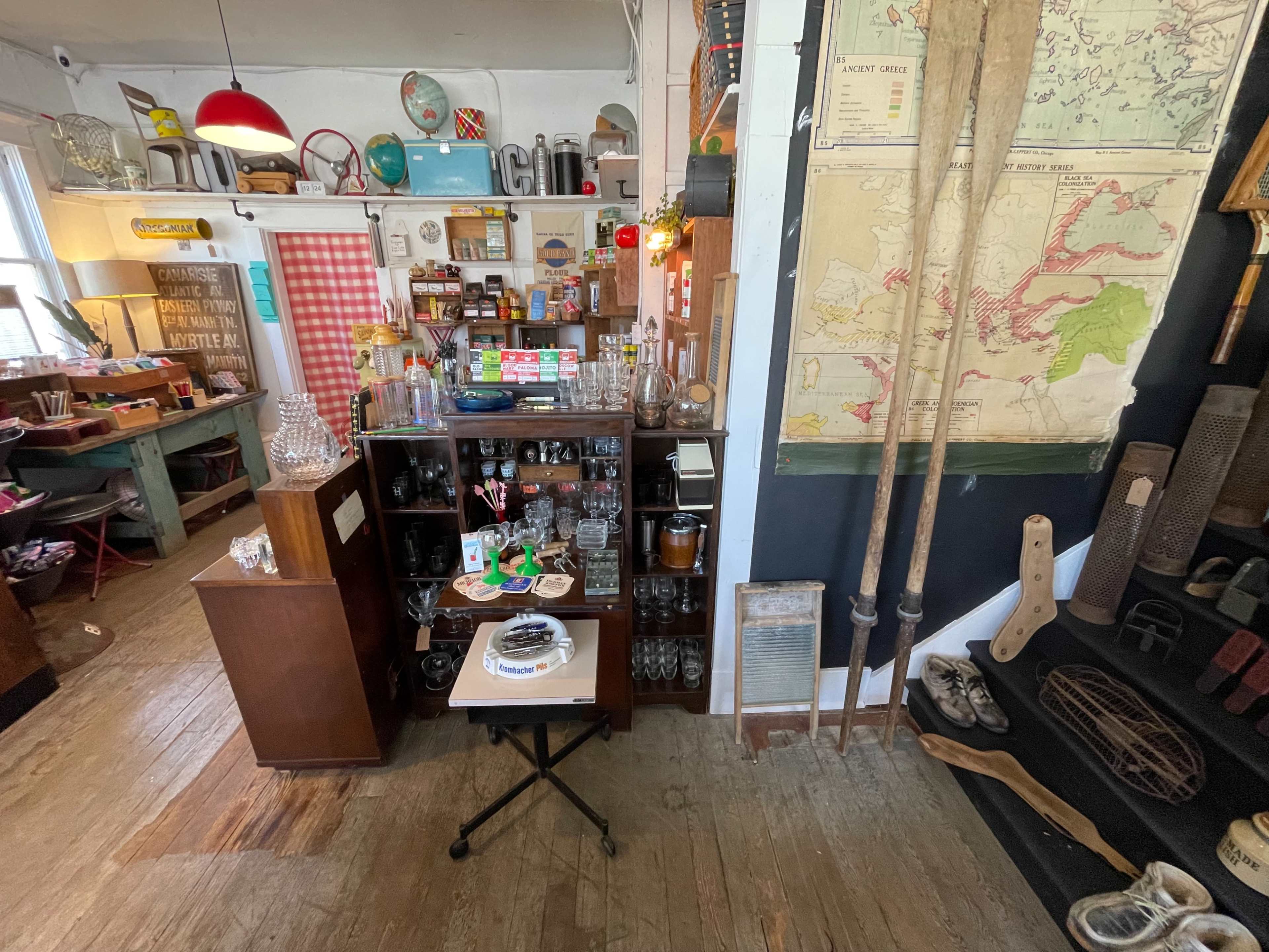 A vintage shop displays various glassware, antiques, and a map along with a small table featuring a cake.