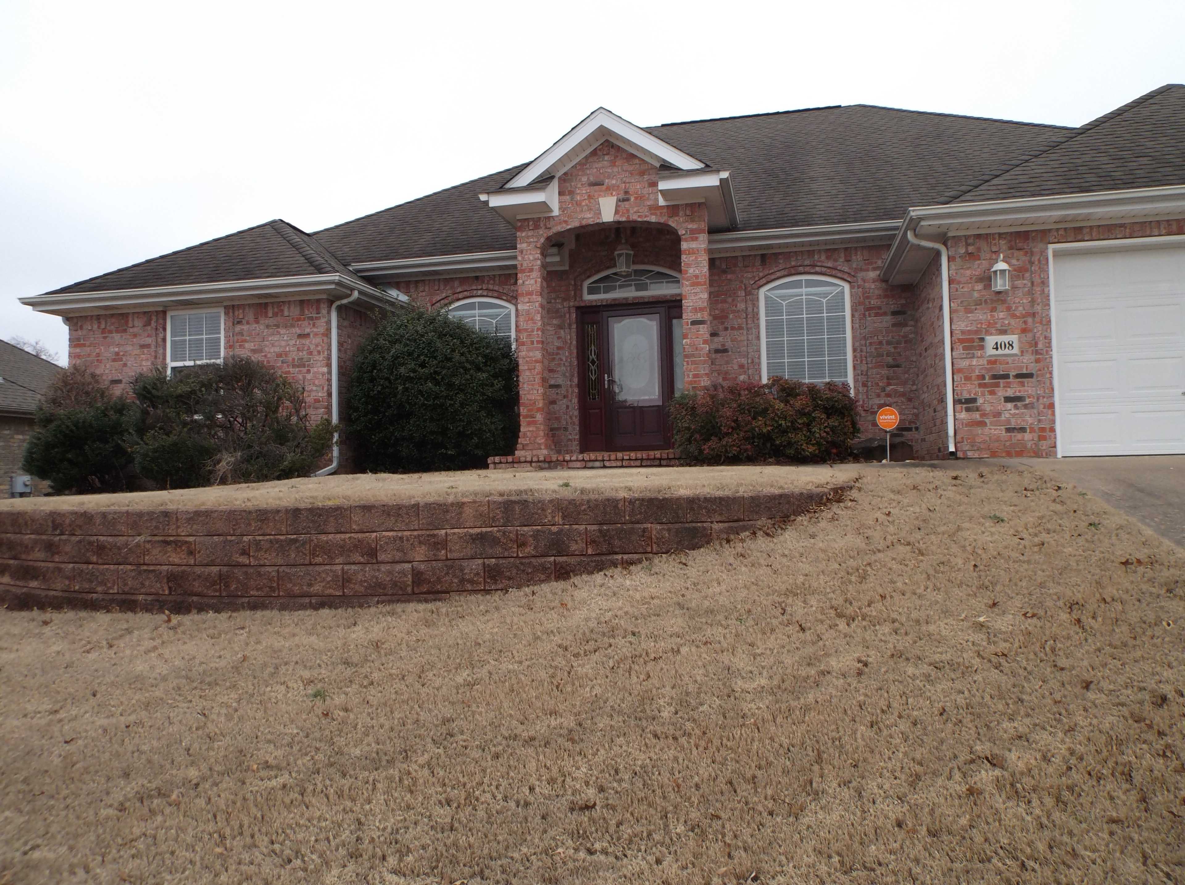 A single-story brick house with a front porch and landscaped yard sits on a gently sloping lot.