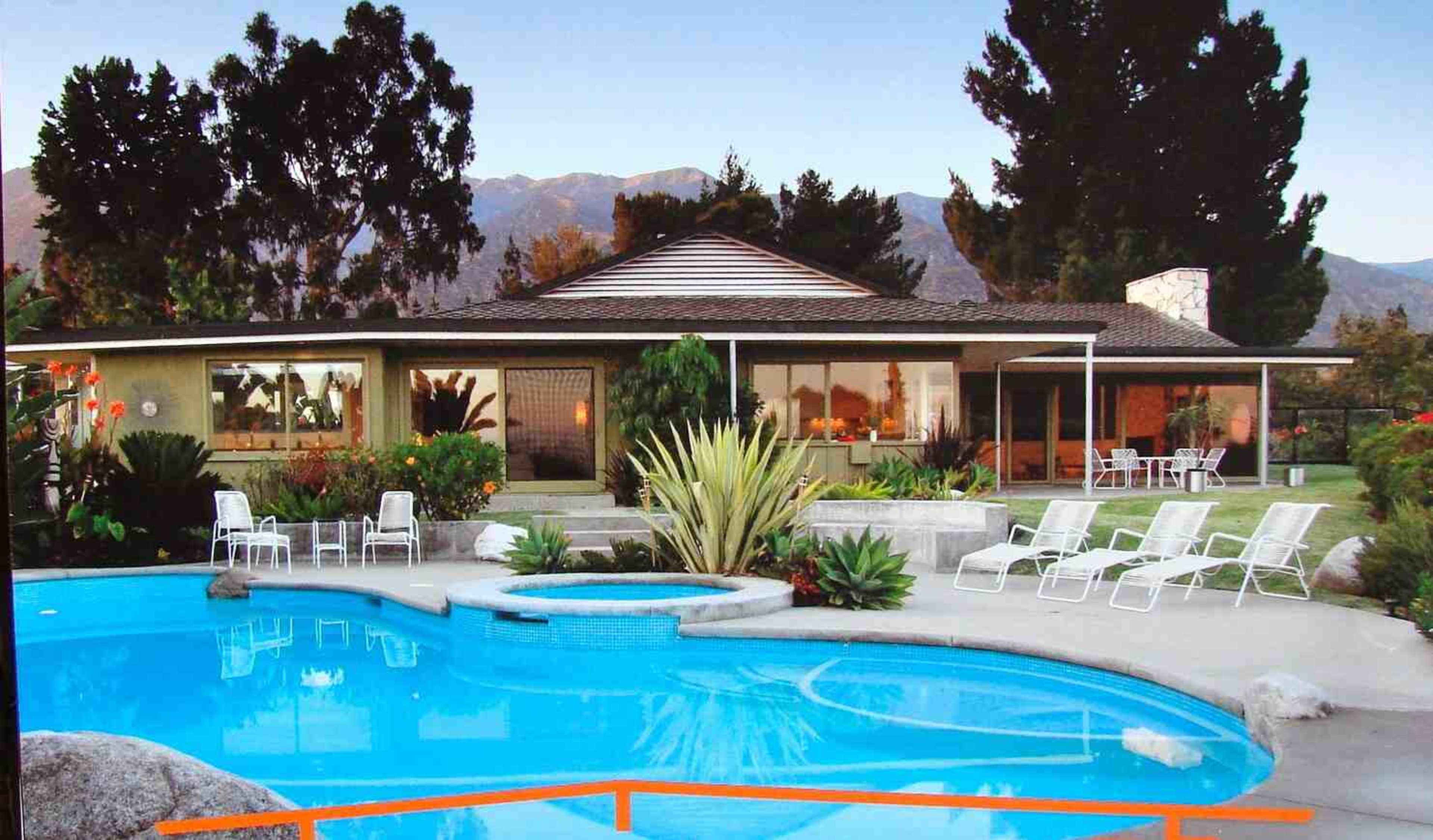 A modern house with large windows, surrounded by a landscaped garden and a swimming pool with lounge chairs.