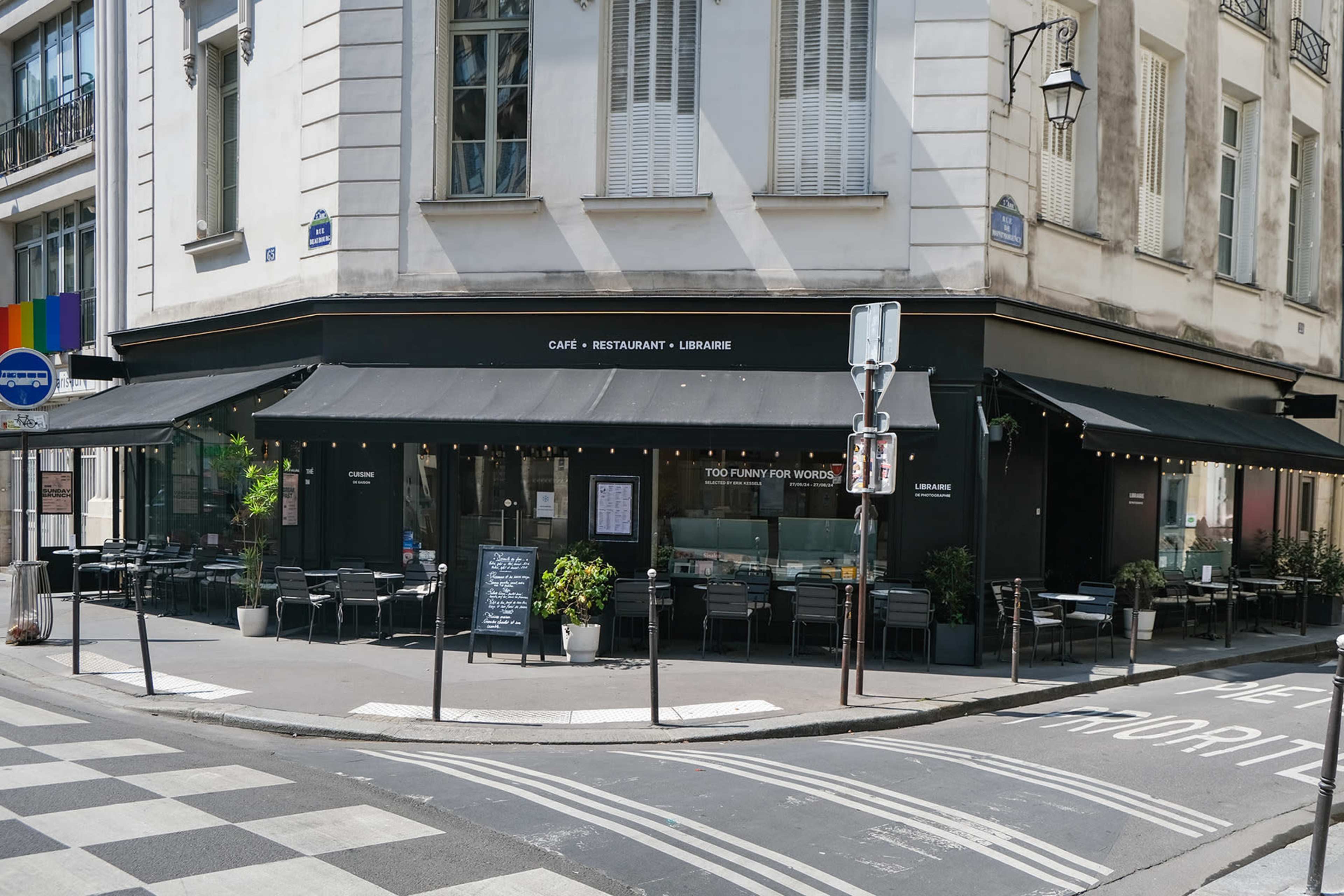 A corner café and restaurant with outdoor seating and large windows is located at the intersection of two streets.