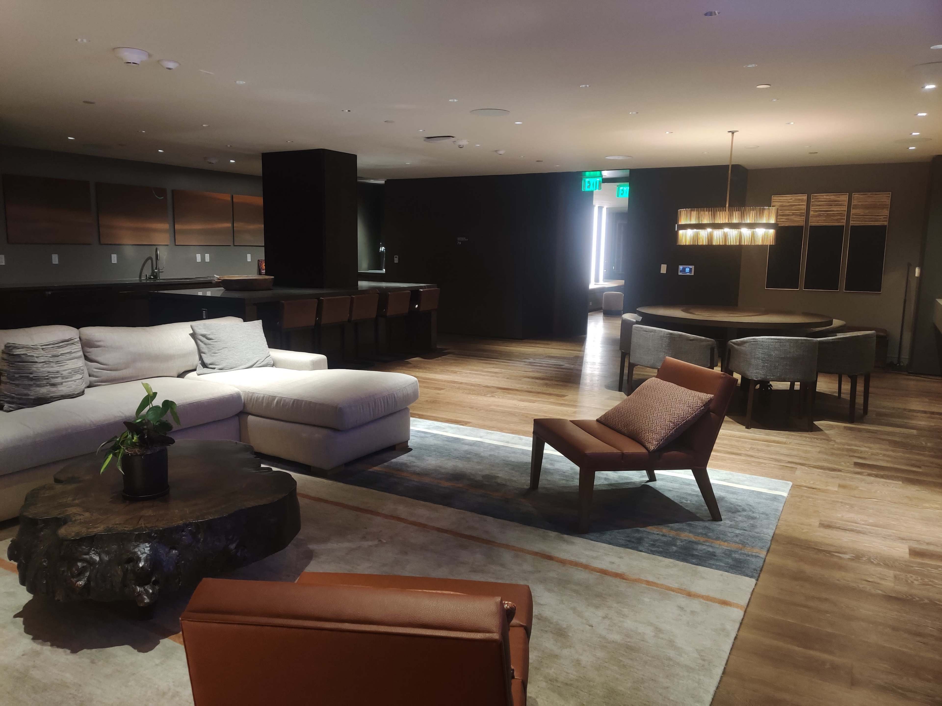 A modern living space with a sectional sofa, a wooden coffee table, a dining area, and large windows allowing natural light to enter.