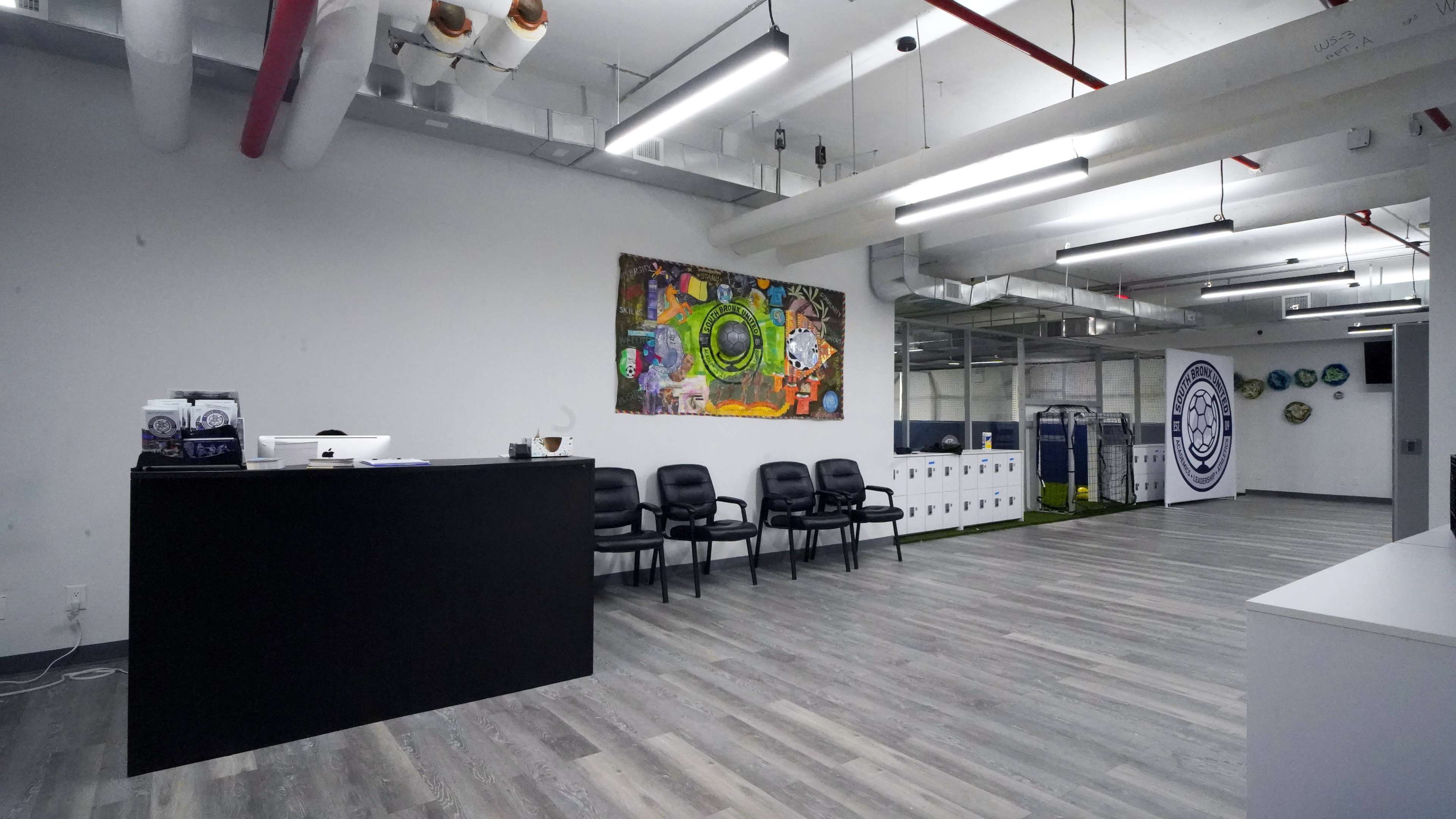 The image shows a modern office interior featuring a receptionist area with a black desk, several black chairs, and a colorful mural on the wall.