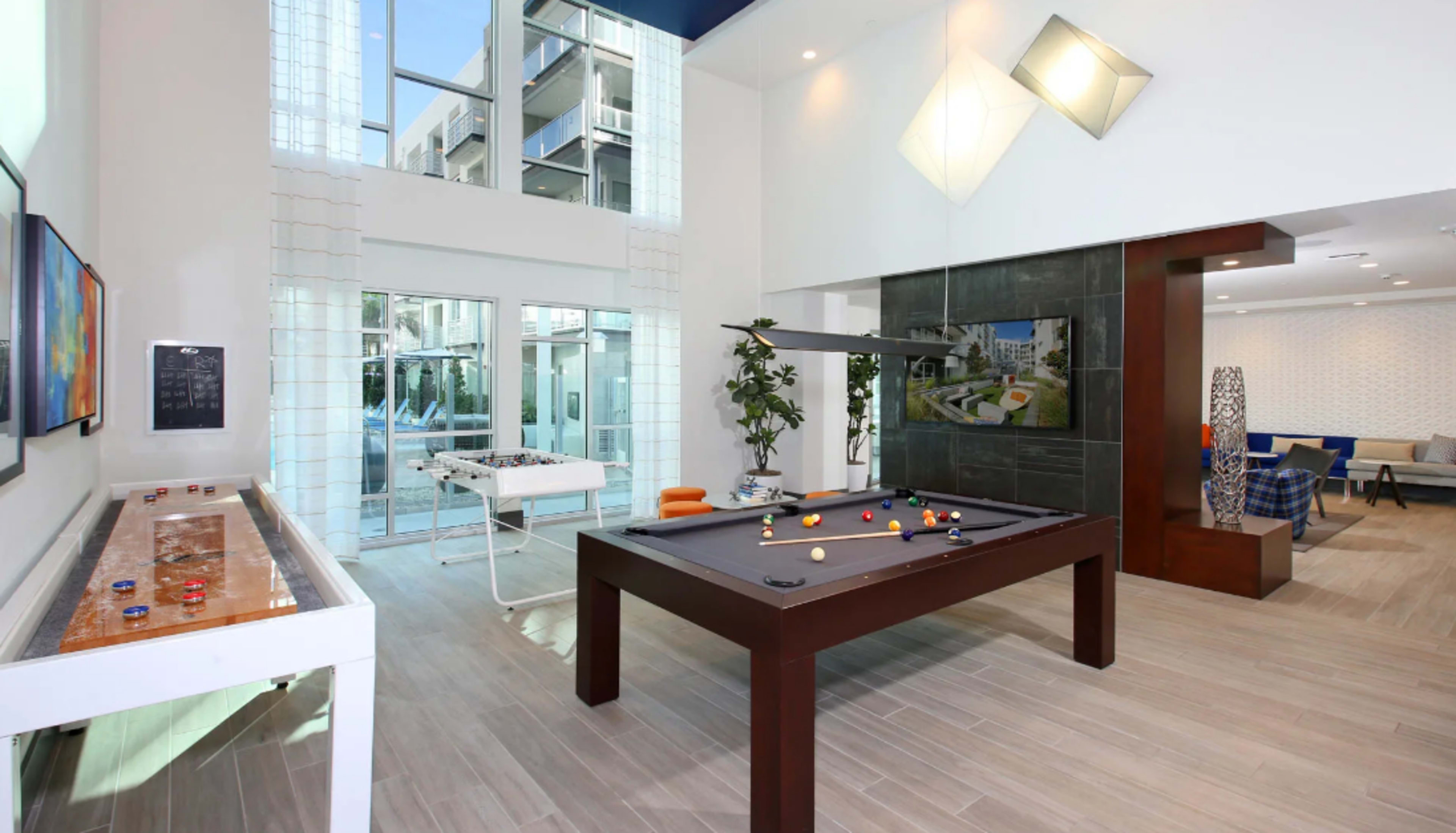 A modern game room featuring a pool table, a foosball table, and large windows that allow natural light into the space.