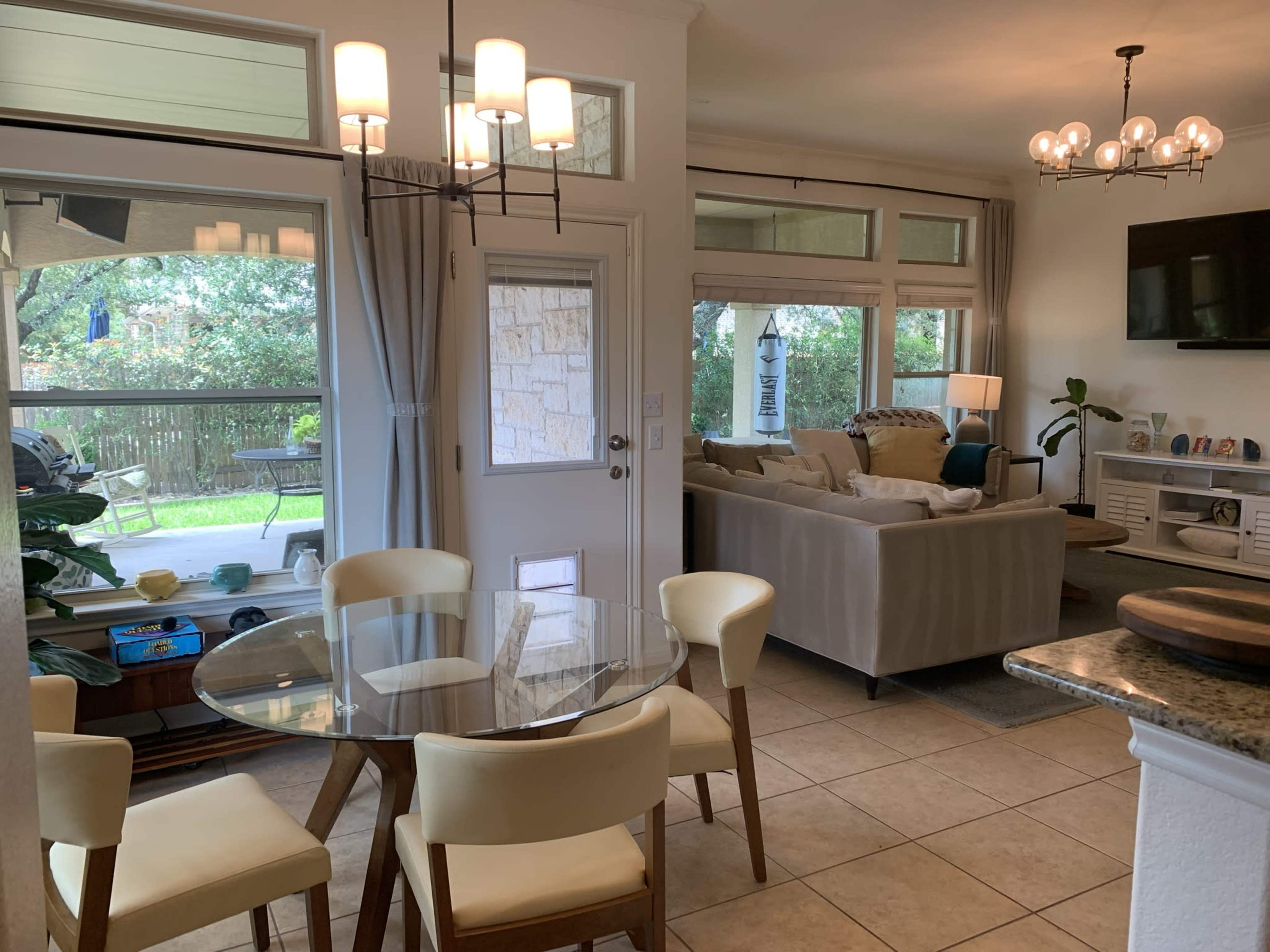 A modern, open-concept living space featuring a dining area with a glass table and four chairs, connected to a cozy living room with a sofa and a television.