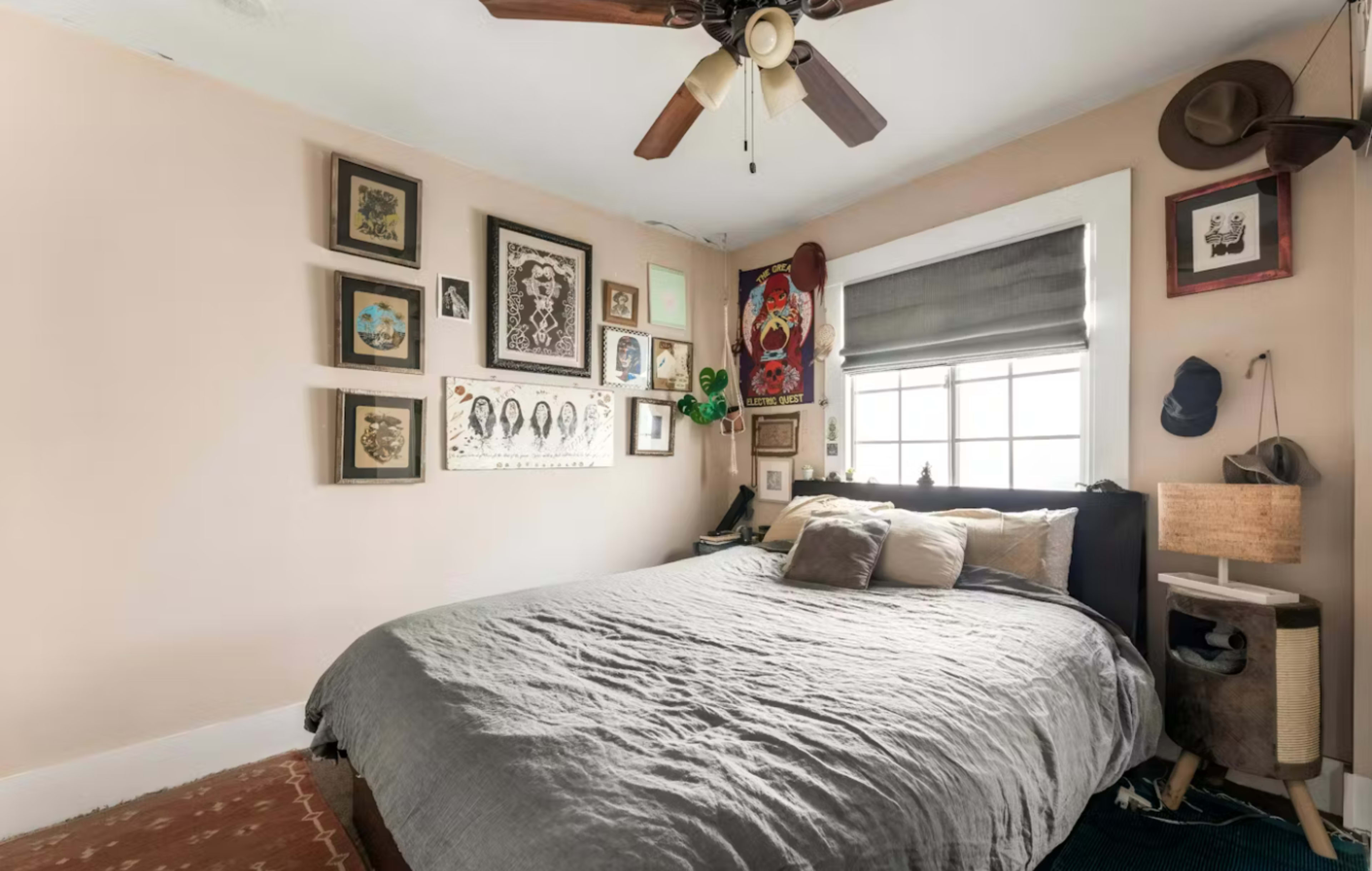 The image shows a cozy bedroom featuring a large bed, adorned with pillows, and surrounded by a collection of framed artwork and photographs on the walls.