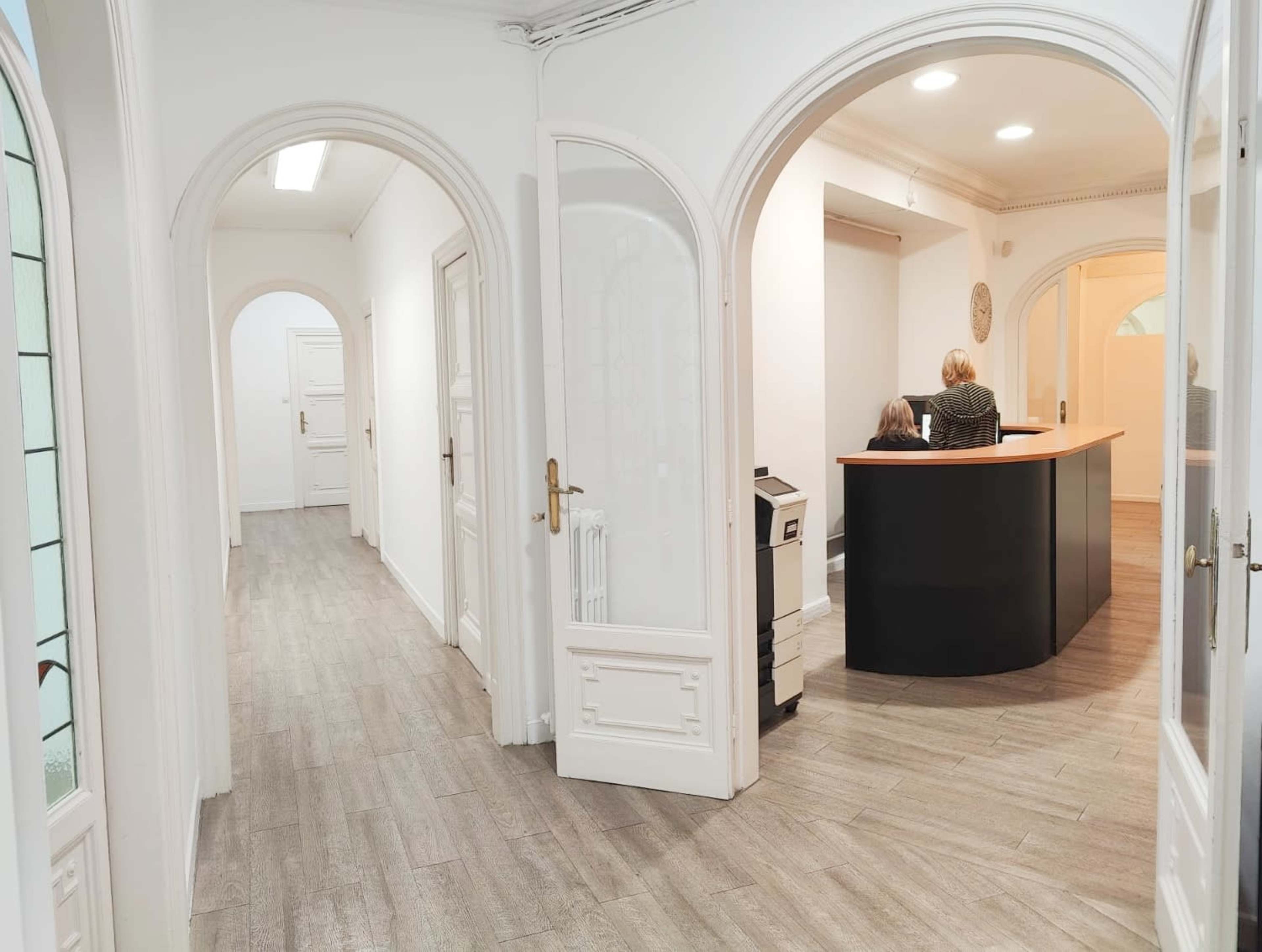 The image shows a well-lit office interior with arched doorways, a reception desk, and a corridor leading to additional rooms.