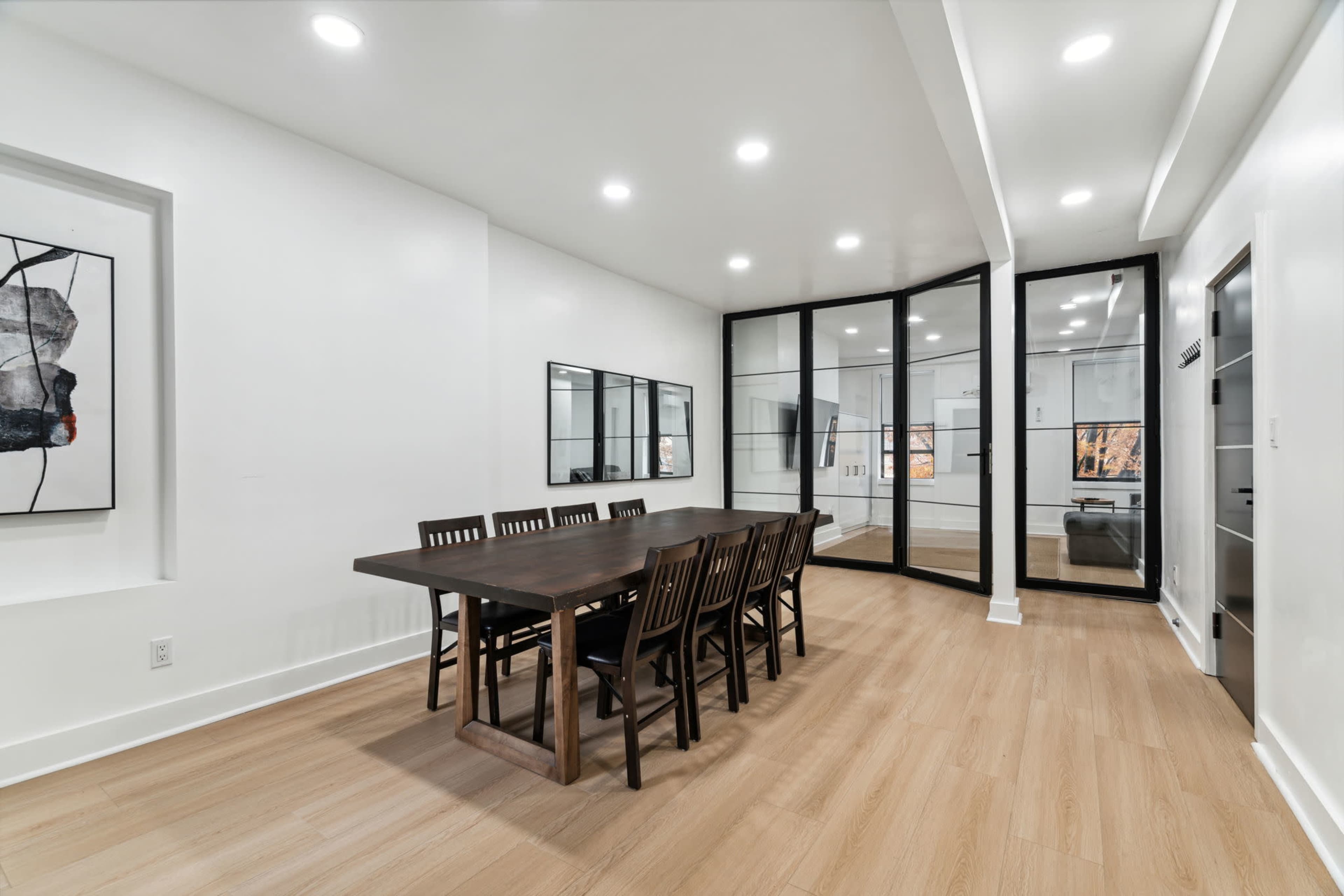A spacious dining area features a large table surrounded by wooden chairs, with glass partitions leading to another room.