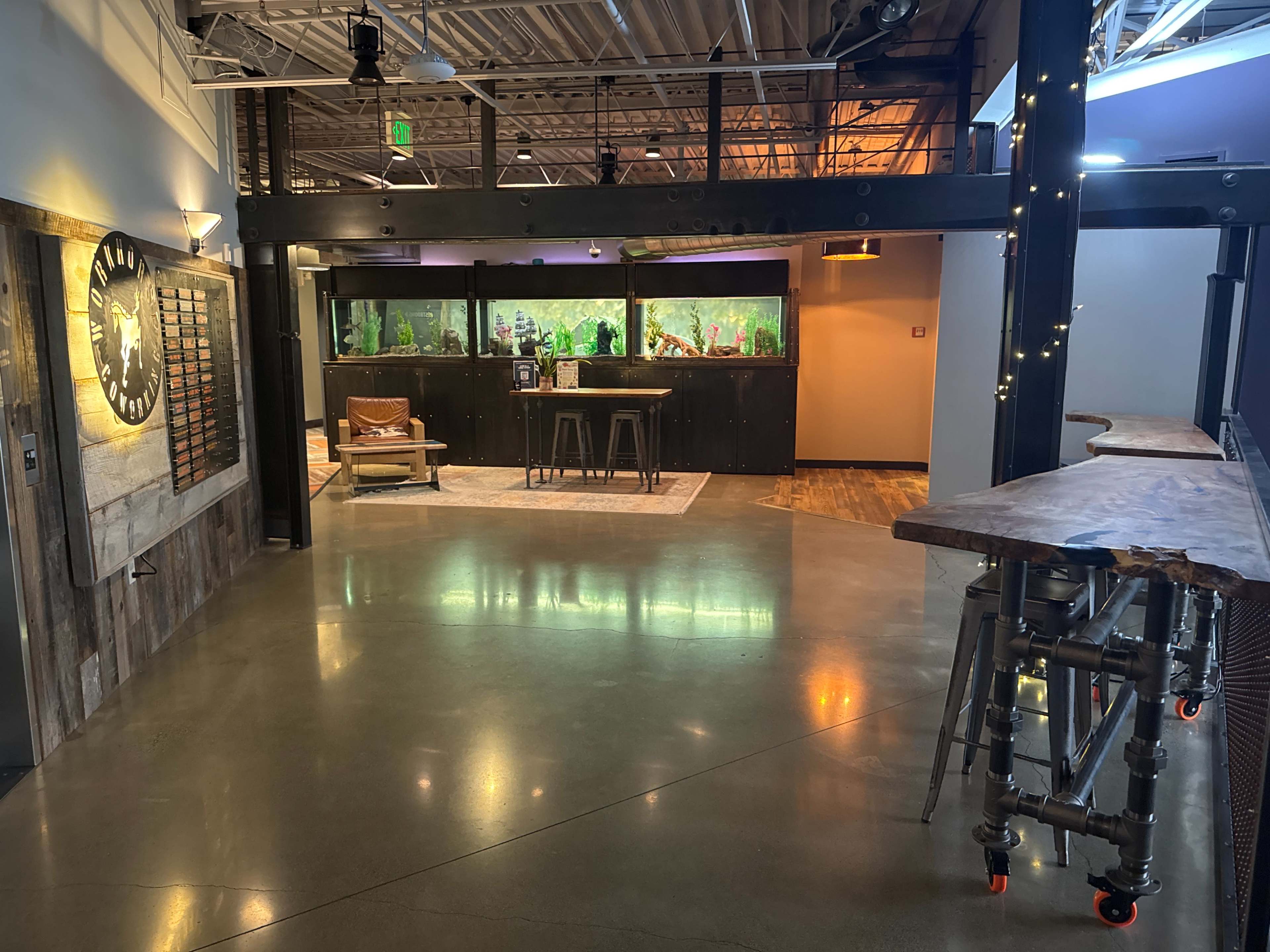 The image shows a spacious interior with polished concrete floors, a bar area with a wooden countertop, and a large aquarium in the background.