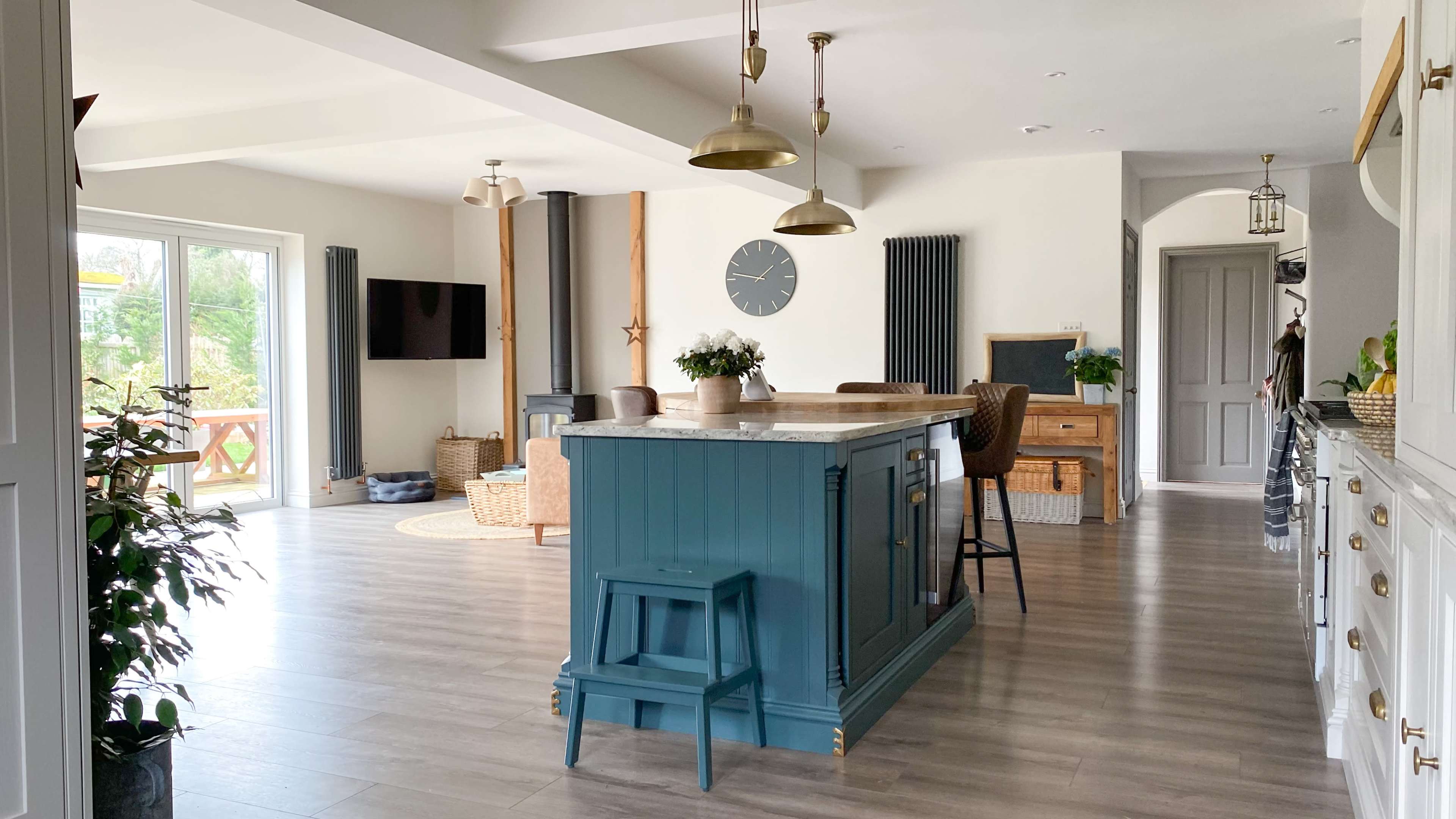A modern open-concept kitchen and living area featuring a central island with a blue base and wooden countertop, surrounded by bar stools and decorated with plants.