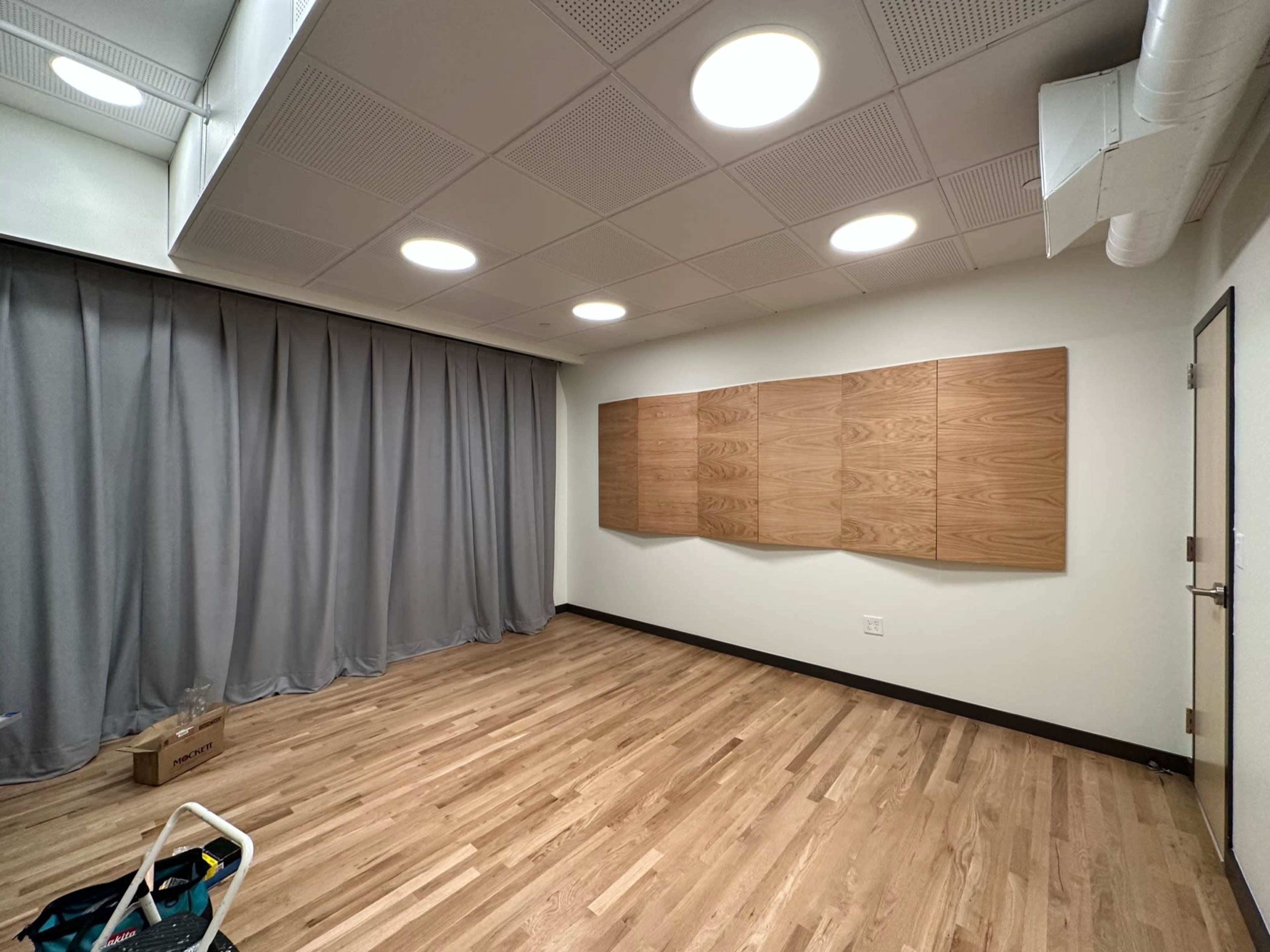 An empty room with wooden flooring, gray curtains on one side, and three wooden panels mounted on the wall.