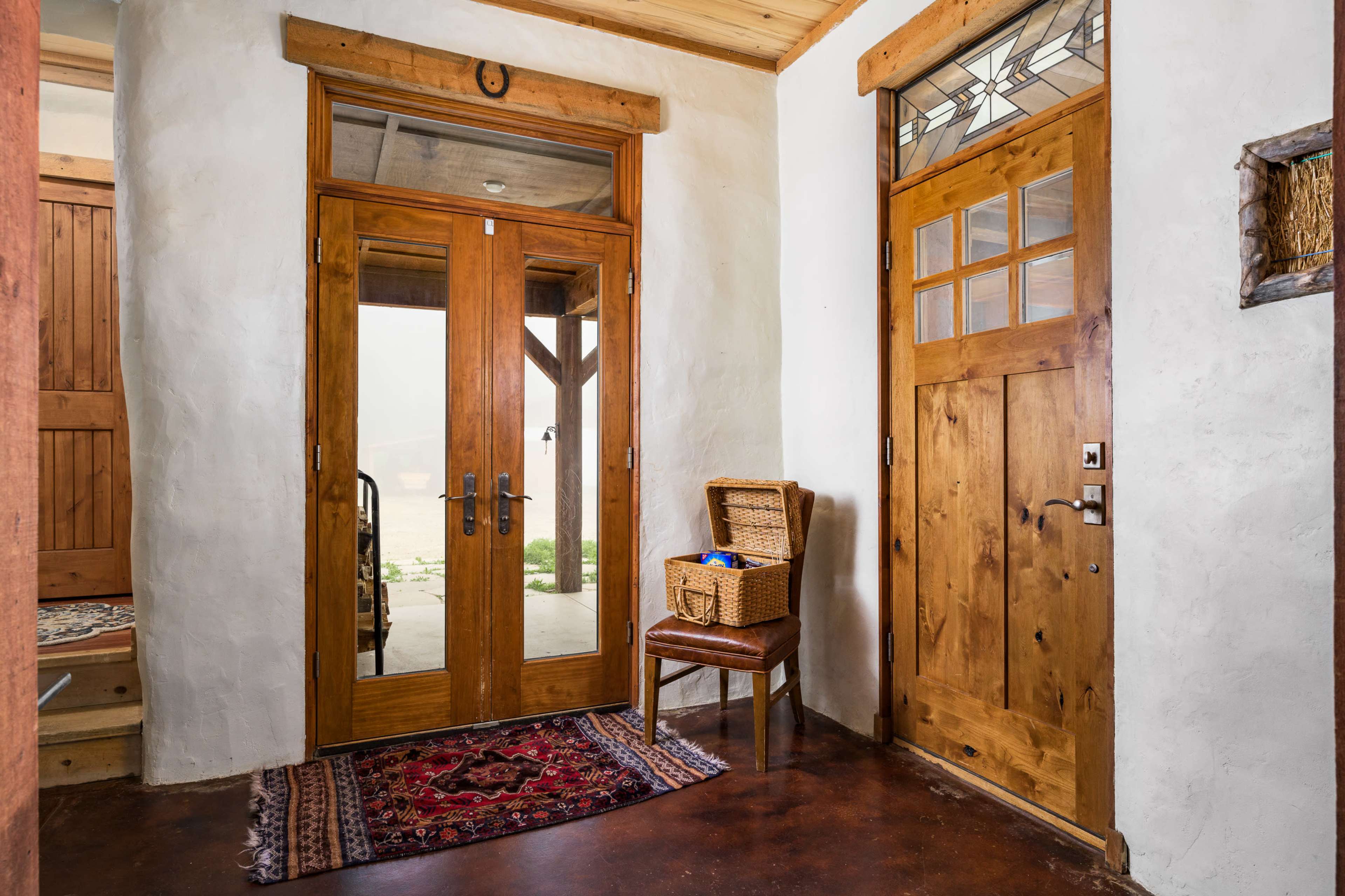 A warmly lit entryway featuring two wooden doors, a wicker basket on a chair, and a patterned rug on the floor.