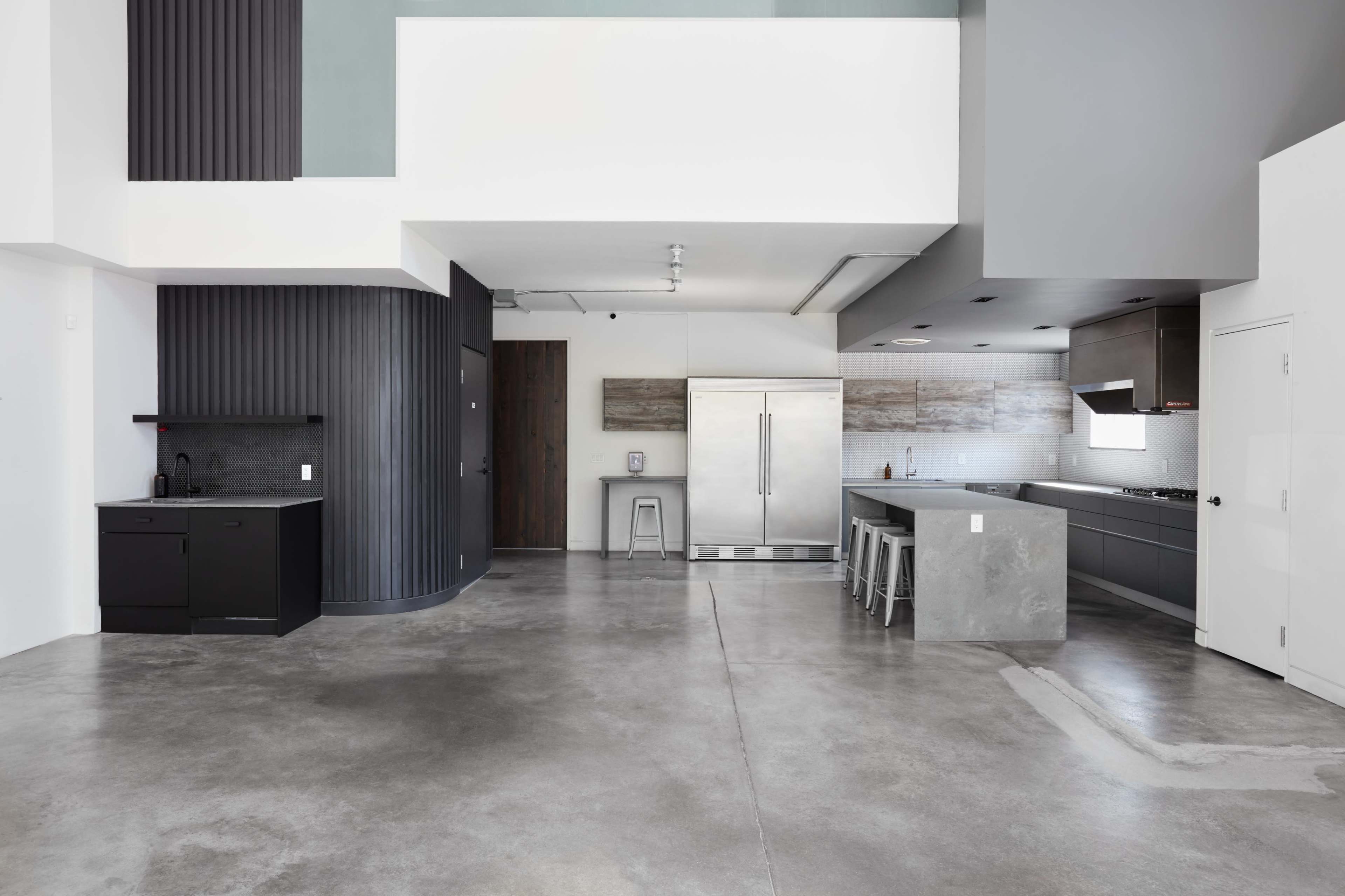 A modern kitchen and dining area with a concrete floor, featuring sleek cabinetry and stainless steel appliances in an open layout.