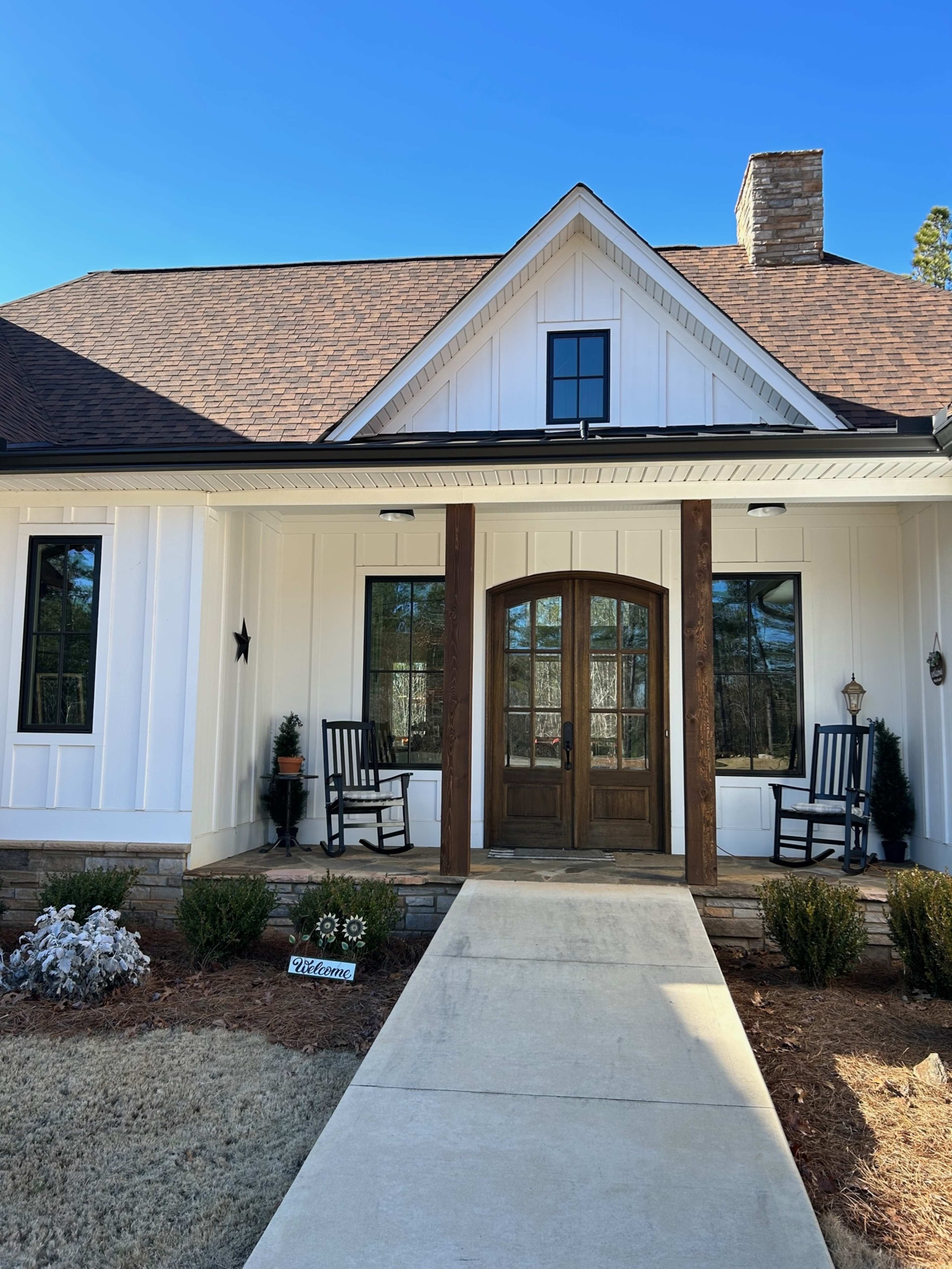 A welcoming front porch of a house with a symmetrical entrance, featuring a wooden double door and two rocking chairs on either side.