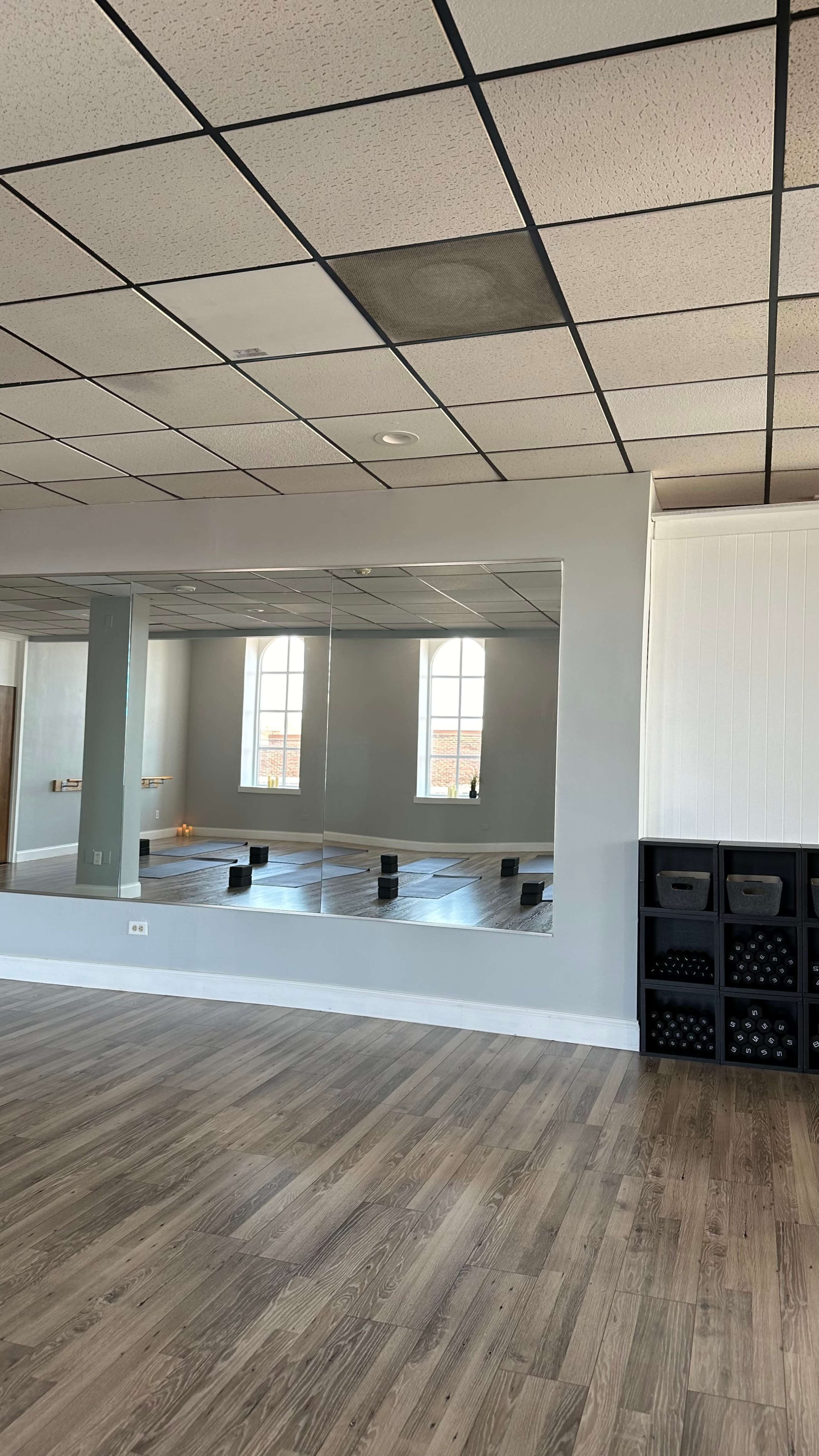 The image shows a spacious, well-lit interior of a studio with a large mirror on one wall and storage boxes stacked on the right.