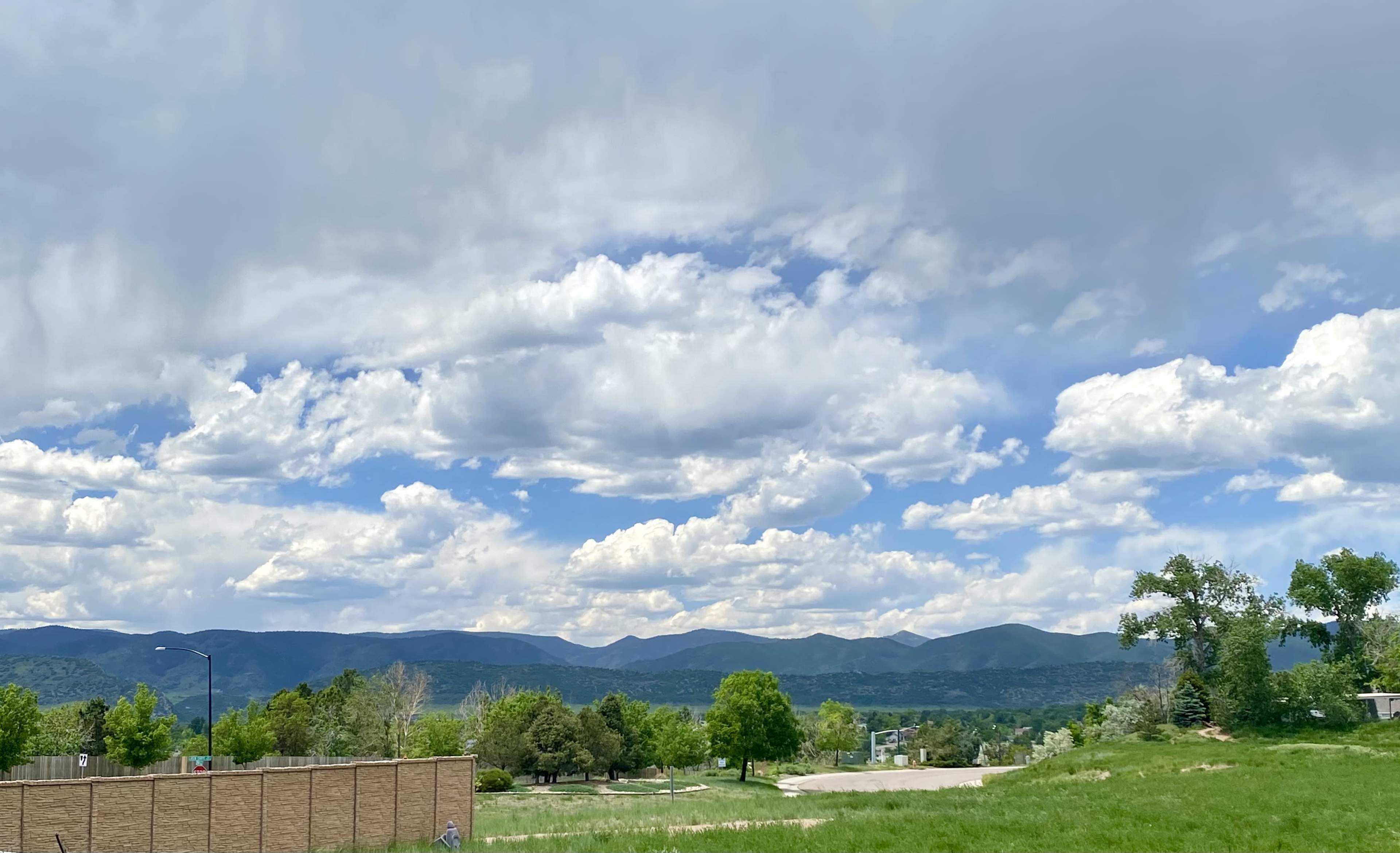 A panoramic view of green fields and mountains under a partly cloudy sky.
