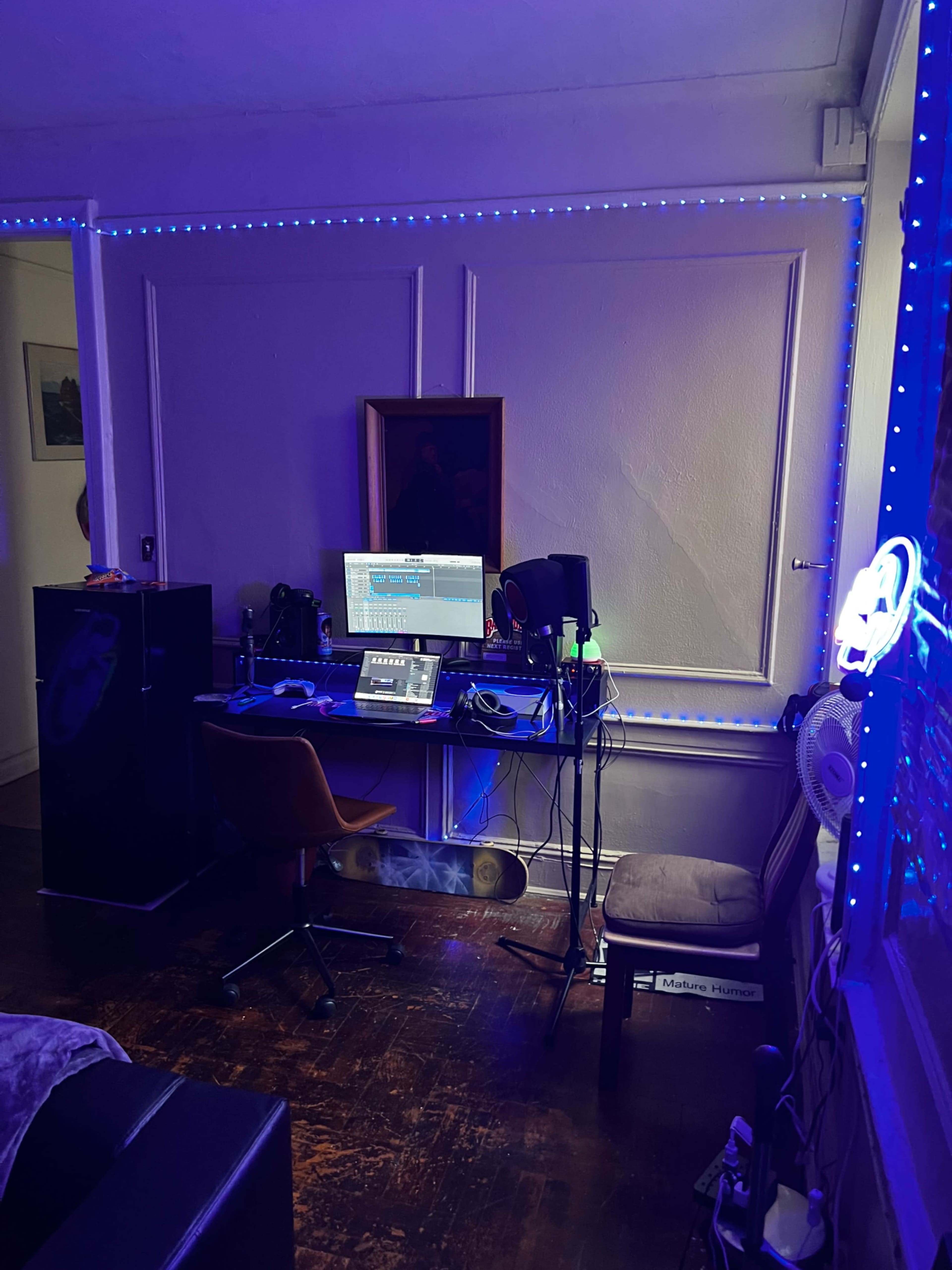 The image shows a room with a desk setup featuring a computer, audio equipment, and purple LED lighting.