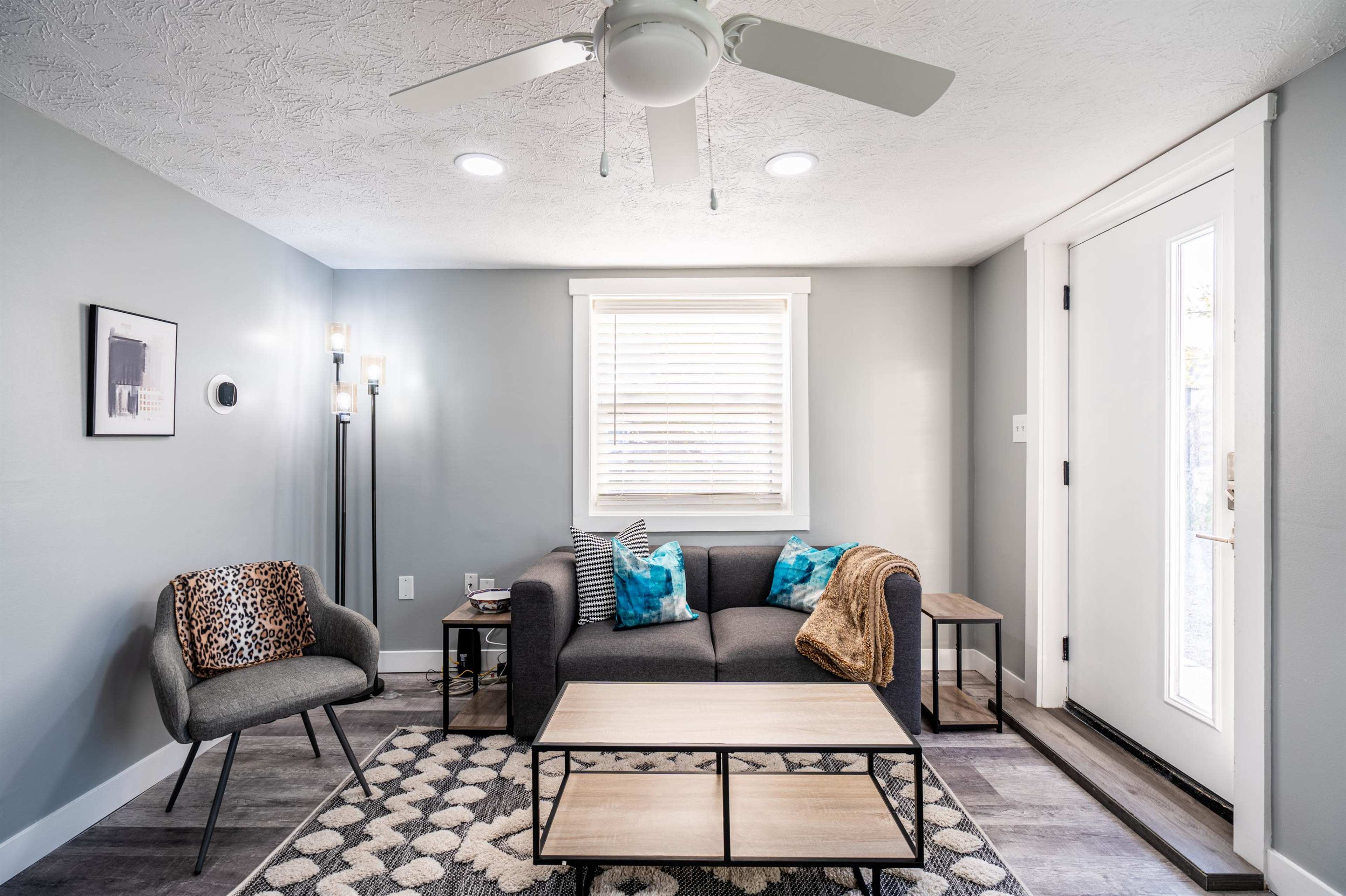 The image shows a modern, minimalistic living room with a gray color scheme, featuring a sofa, a coffee table, and a door leading outside.